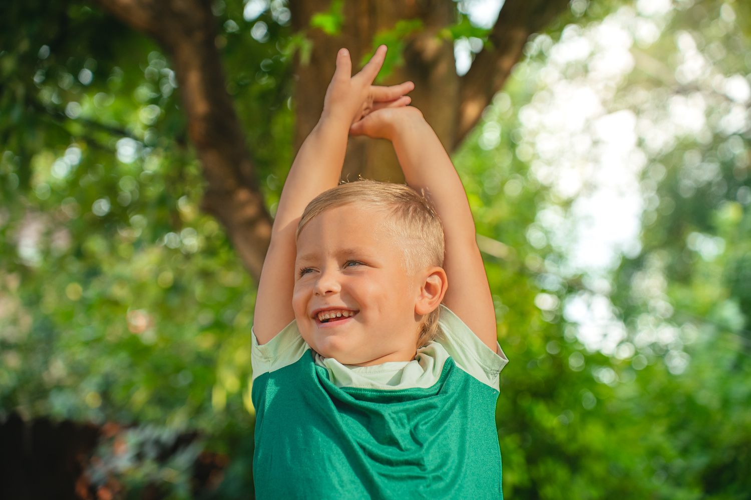 A child in a green shirt plays joyfully outdoors in natural lighting.