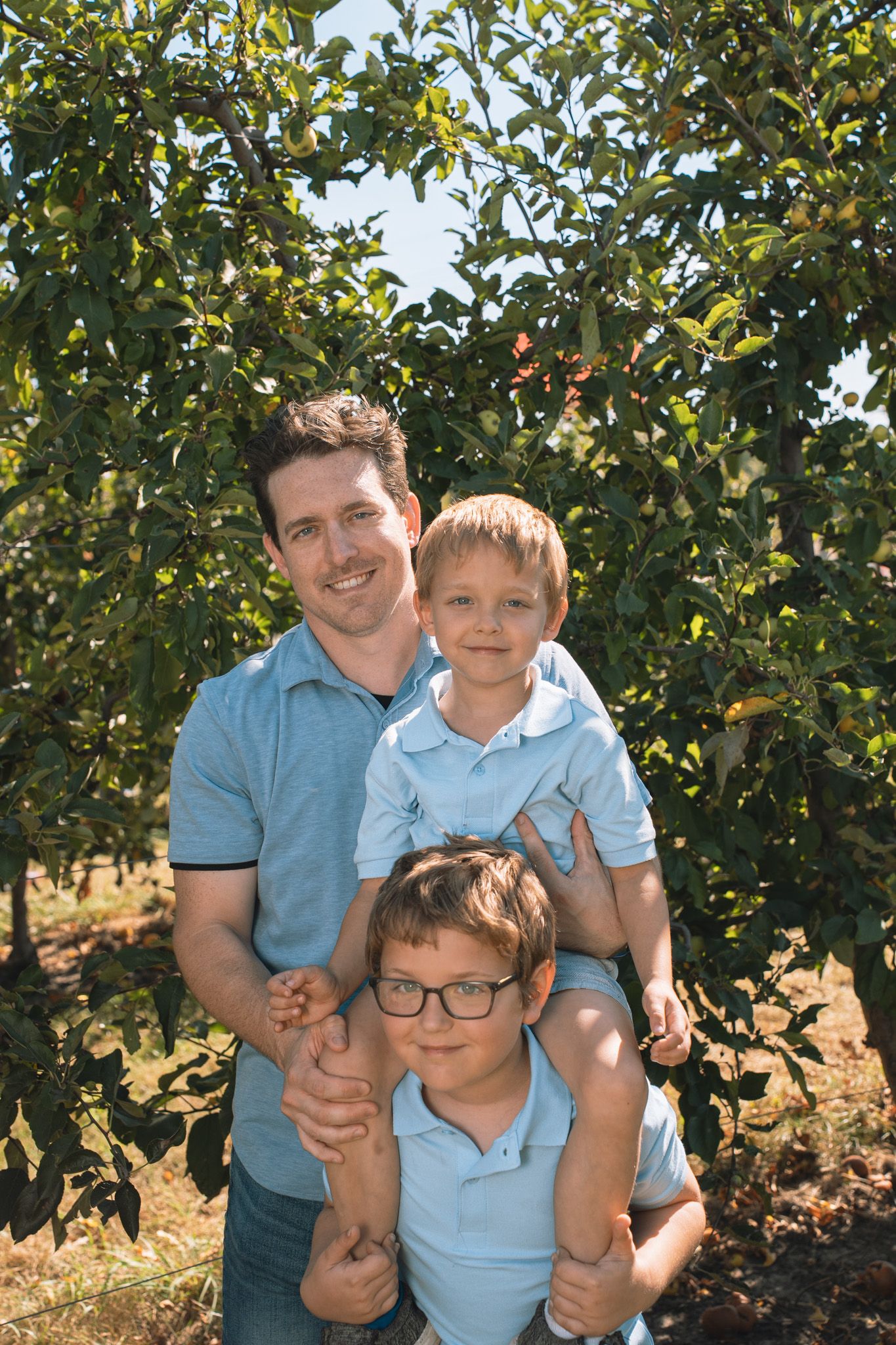 Family group wearing matching blue shirts posing among apple trees.