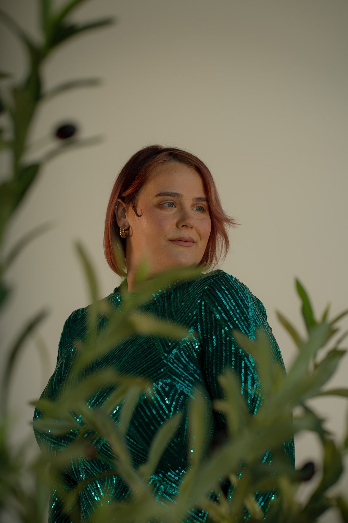 Sparkly green sequined dress framed by indoor plants in soft lighting.