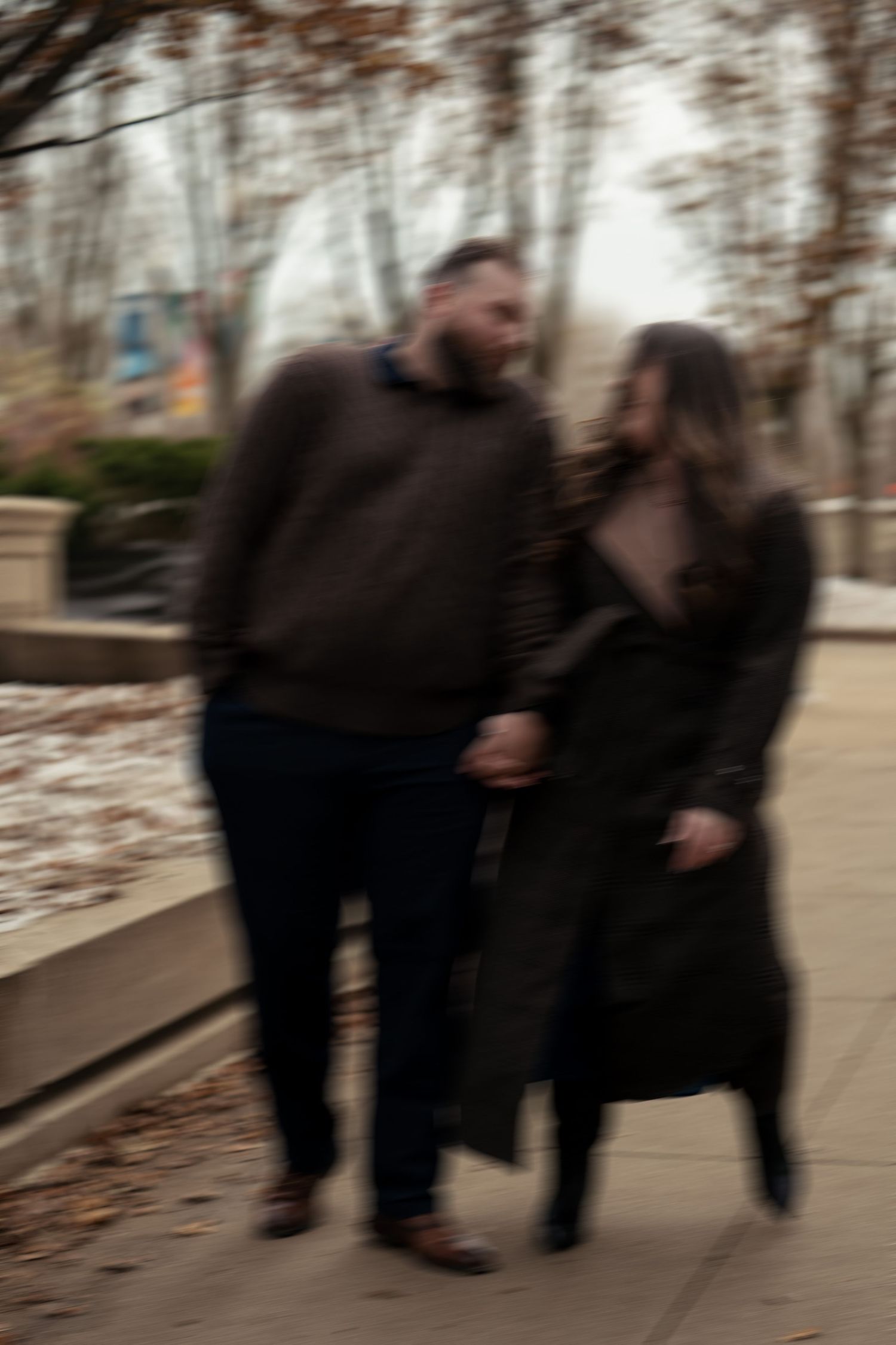 A couple walking together on a path through bare trees on an autumn day, captured with motion blur effect.
