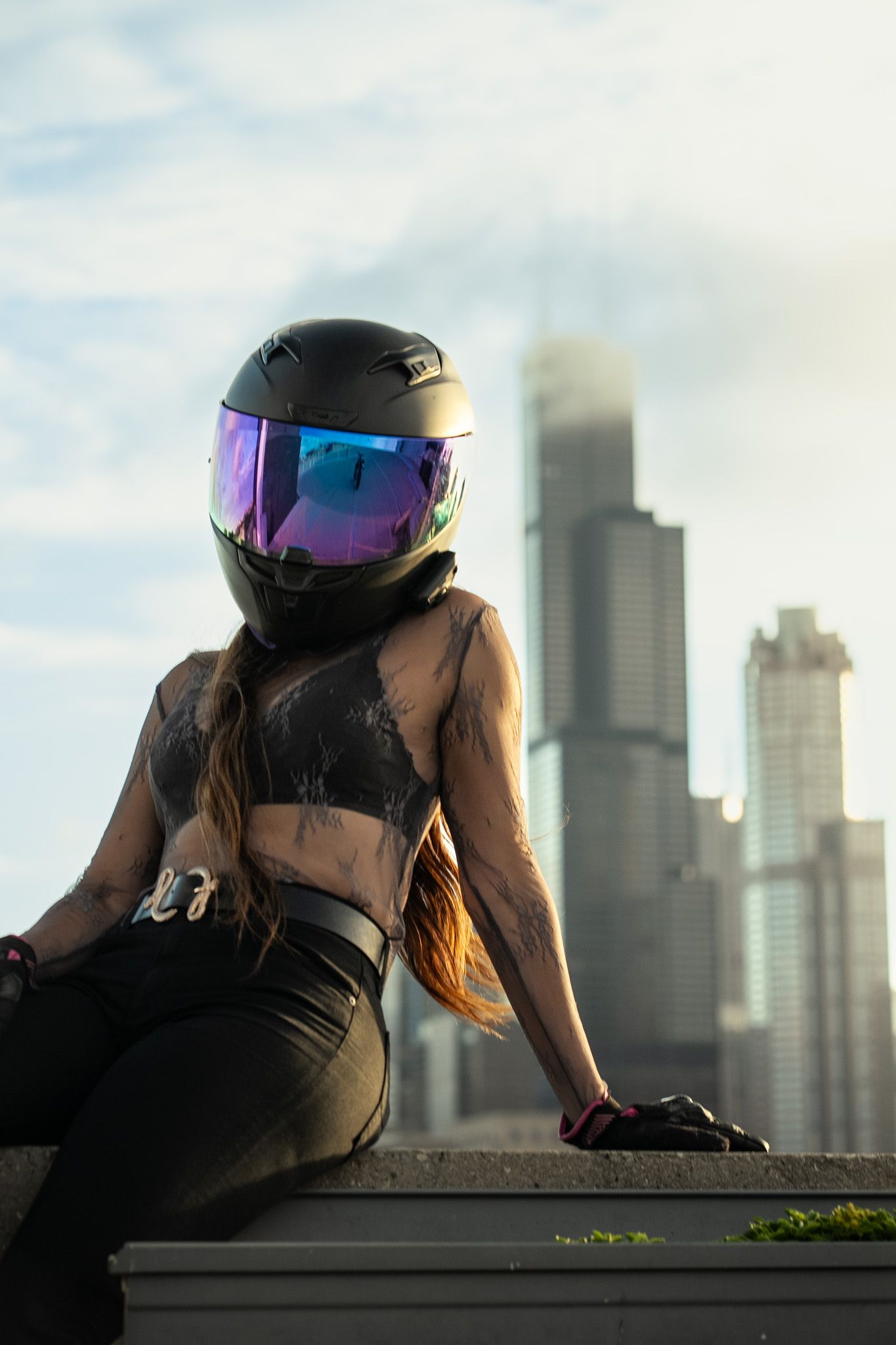 Motorcyclist wearing black helmet with iridescent visor sits against city backdrop.