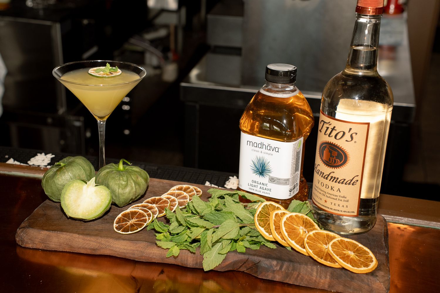 Bar setup with cocktail ingredients including citrus slices, herbs, and various liquor bottles.