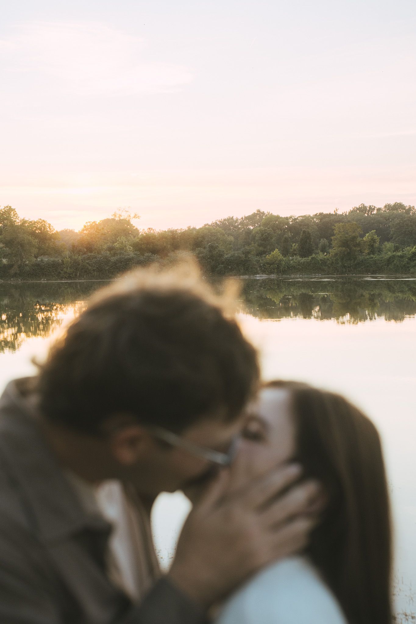Romantic couple sharing an intimate moment by a serene lake at sunset.