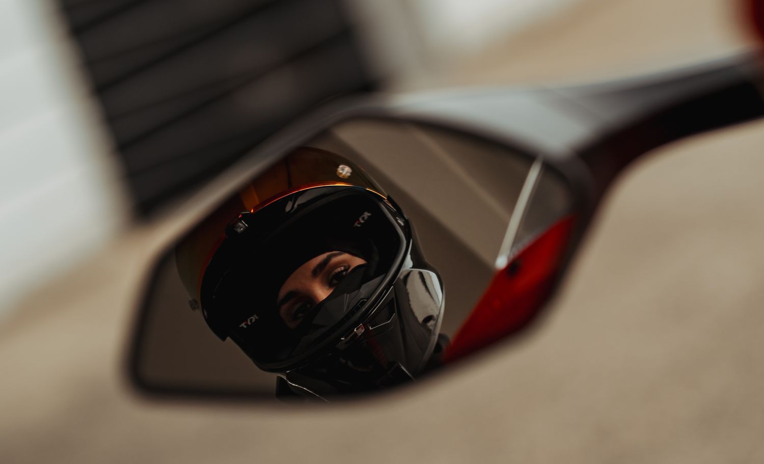Motorcycle rider reflected in a rearview mirror wearing a helmet, captured in a close-up shot.