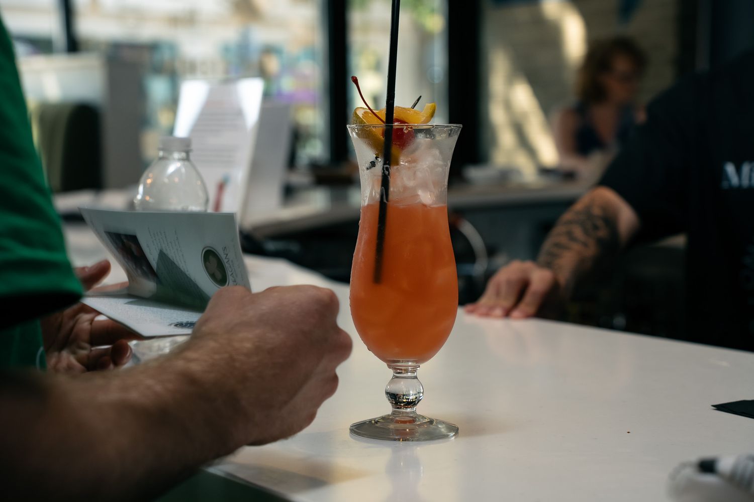 Hands reaching for colorful cocktails on a white table at a bar.