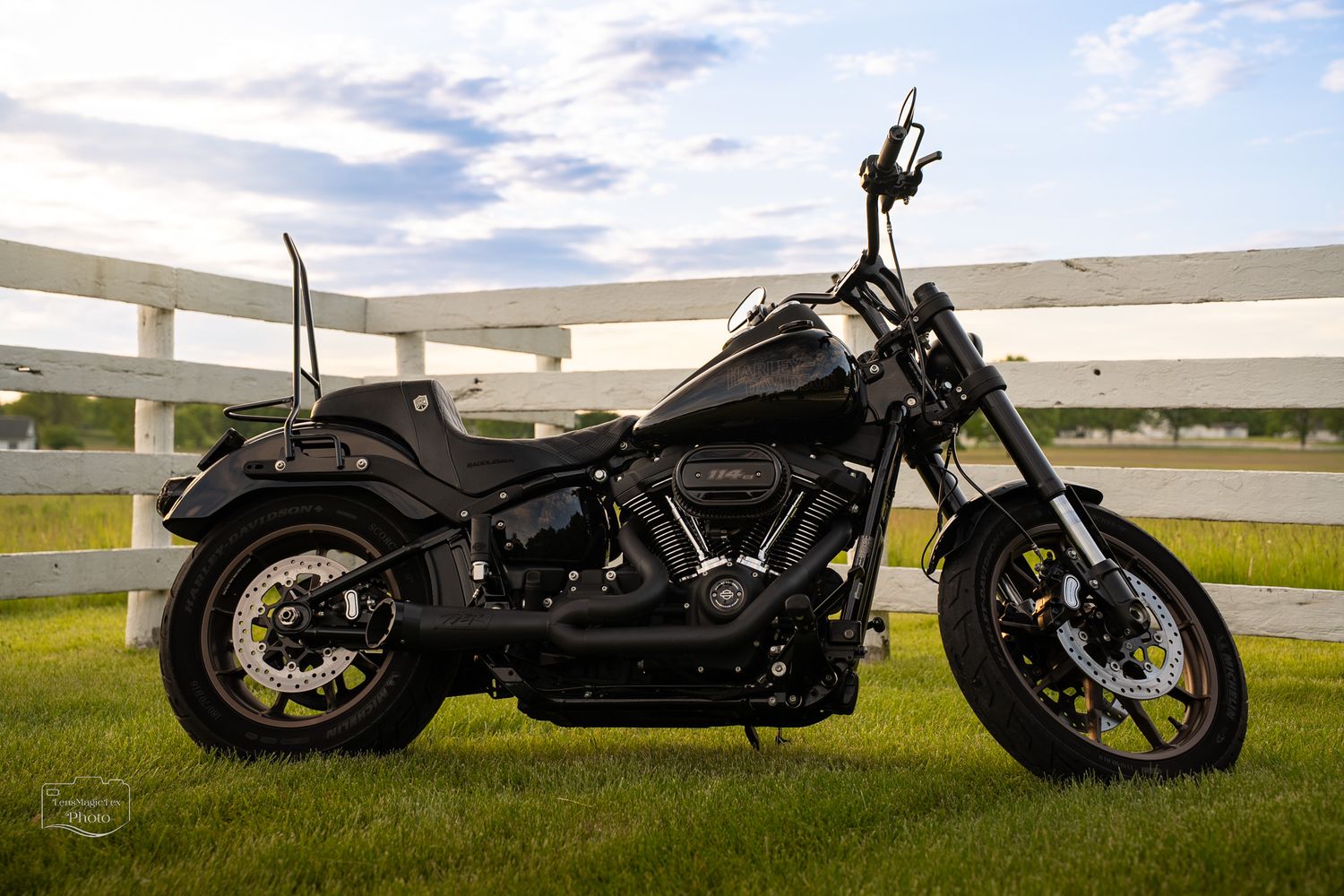 Low angle view of dark motorcycles parked on grass against cloudy sky.