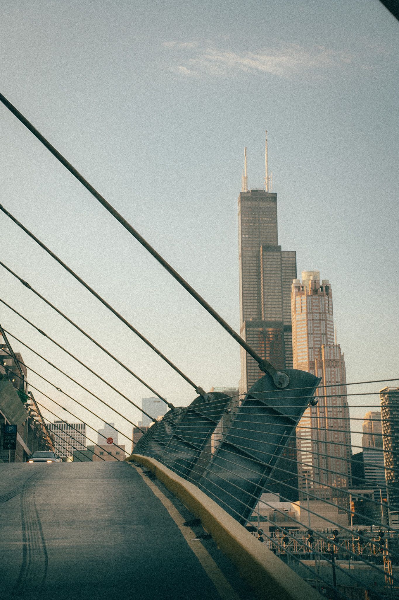 Modern architectural view of Chicago's Willis Tower through bridge cables against a blue sky.