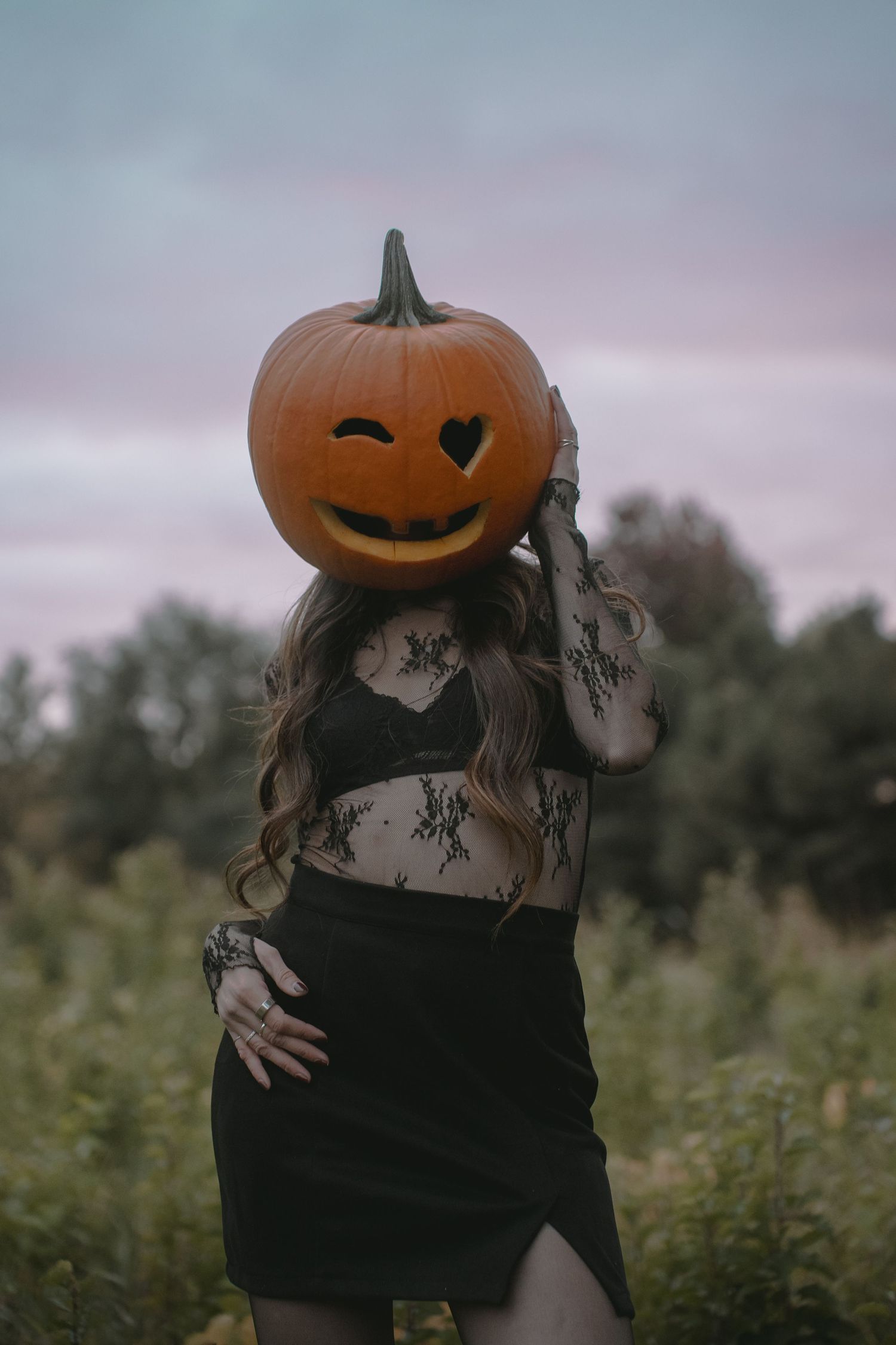 A mysterious figure in black clothing with a carved pumpkin head stands in a misty outdoor setting.