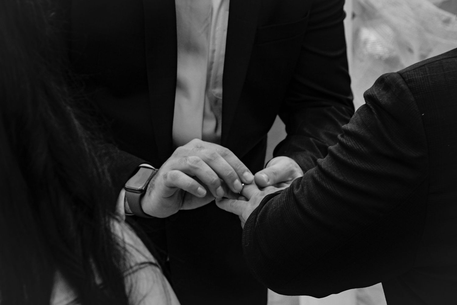 Artistic black and white detail shot of hands during a ring exchange.