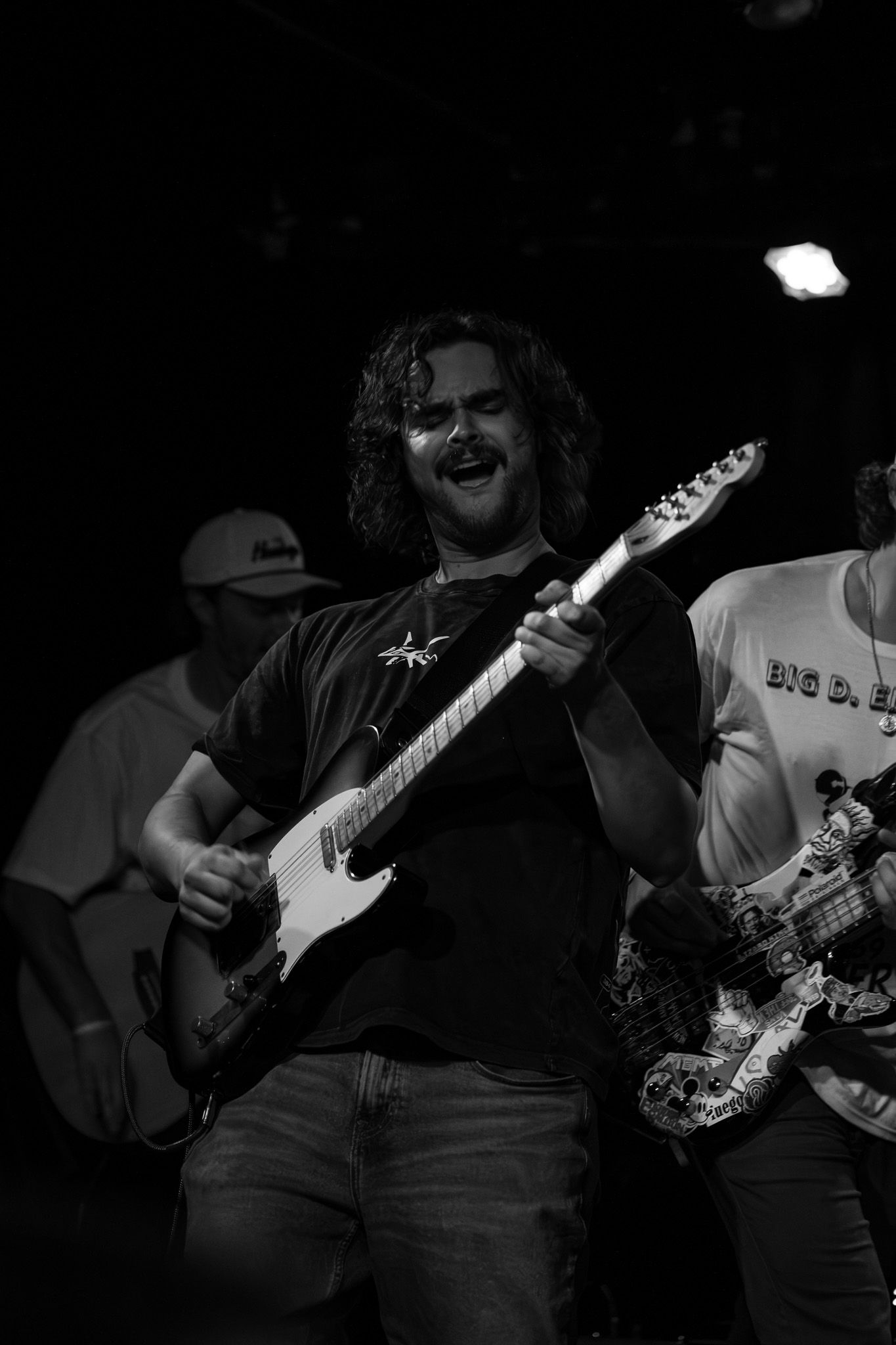 Band members playing electric guitars during a dimly lit live performance.