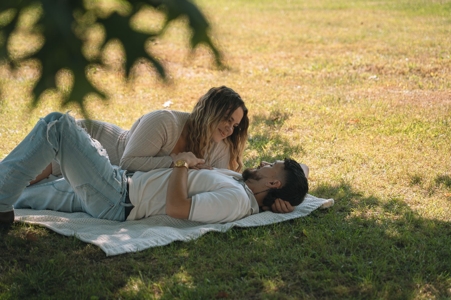 A couple lies together on grass during a sunny outdoor photoshoot.