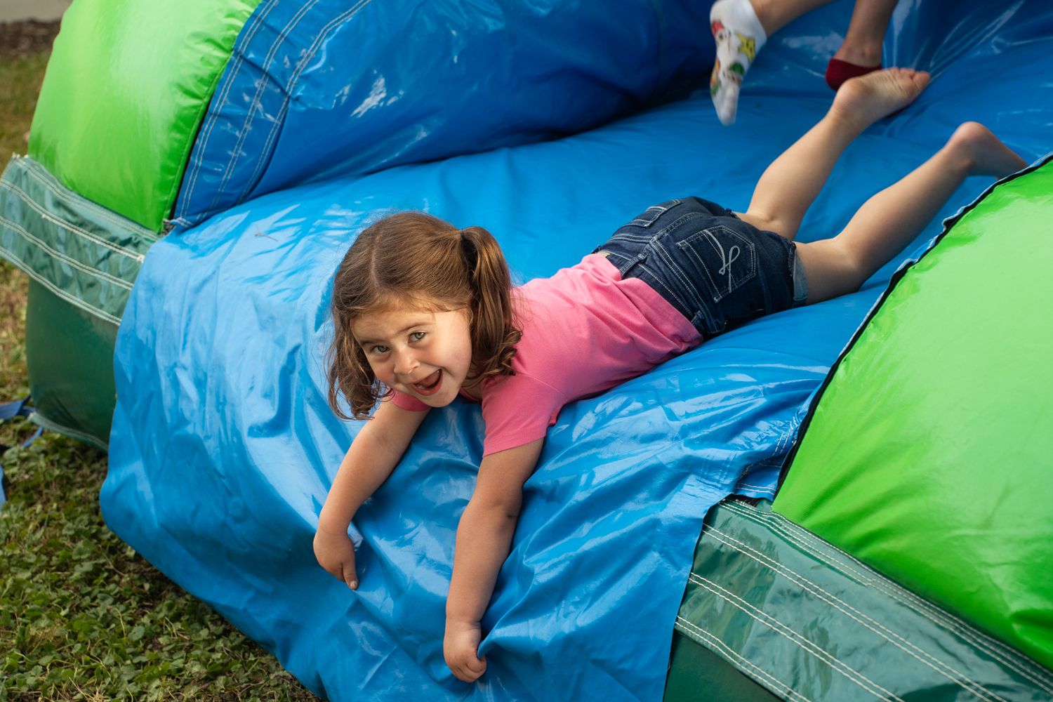Children bouncing and playing on a blue and green inflatable bounce house.