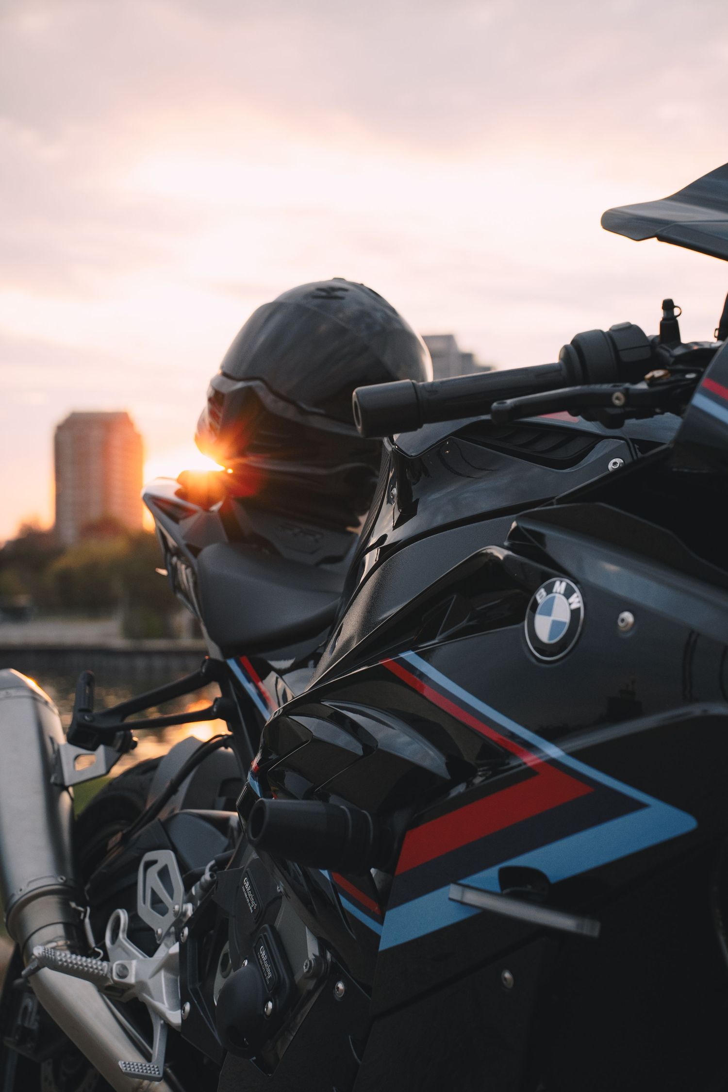 BMW motorcycle with racing stripes photographed at sunset with a building silhouette.