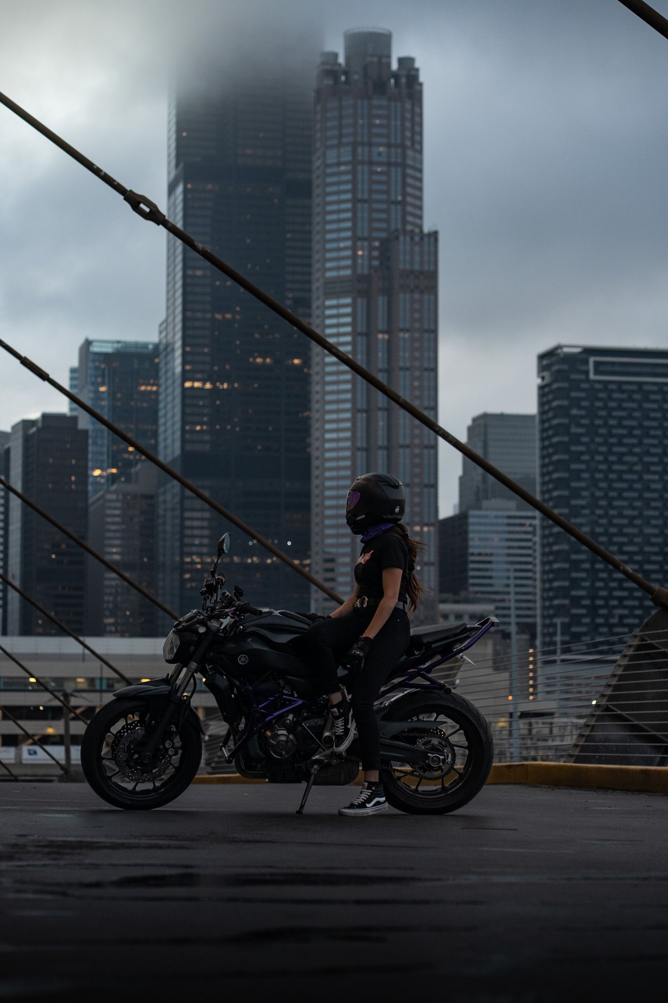 Motorcycles lined up on a bridge with dramatic urban skyline and stormy clouds in the background.