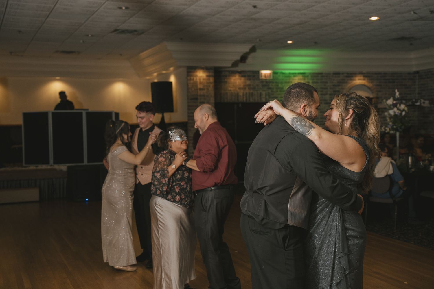 Couples slow dancing together on a dimly lit dance floor at an evening event.