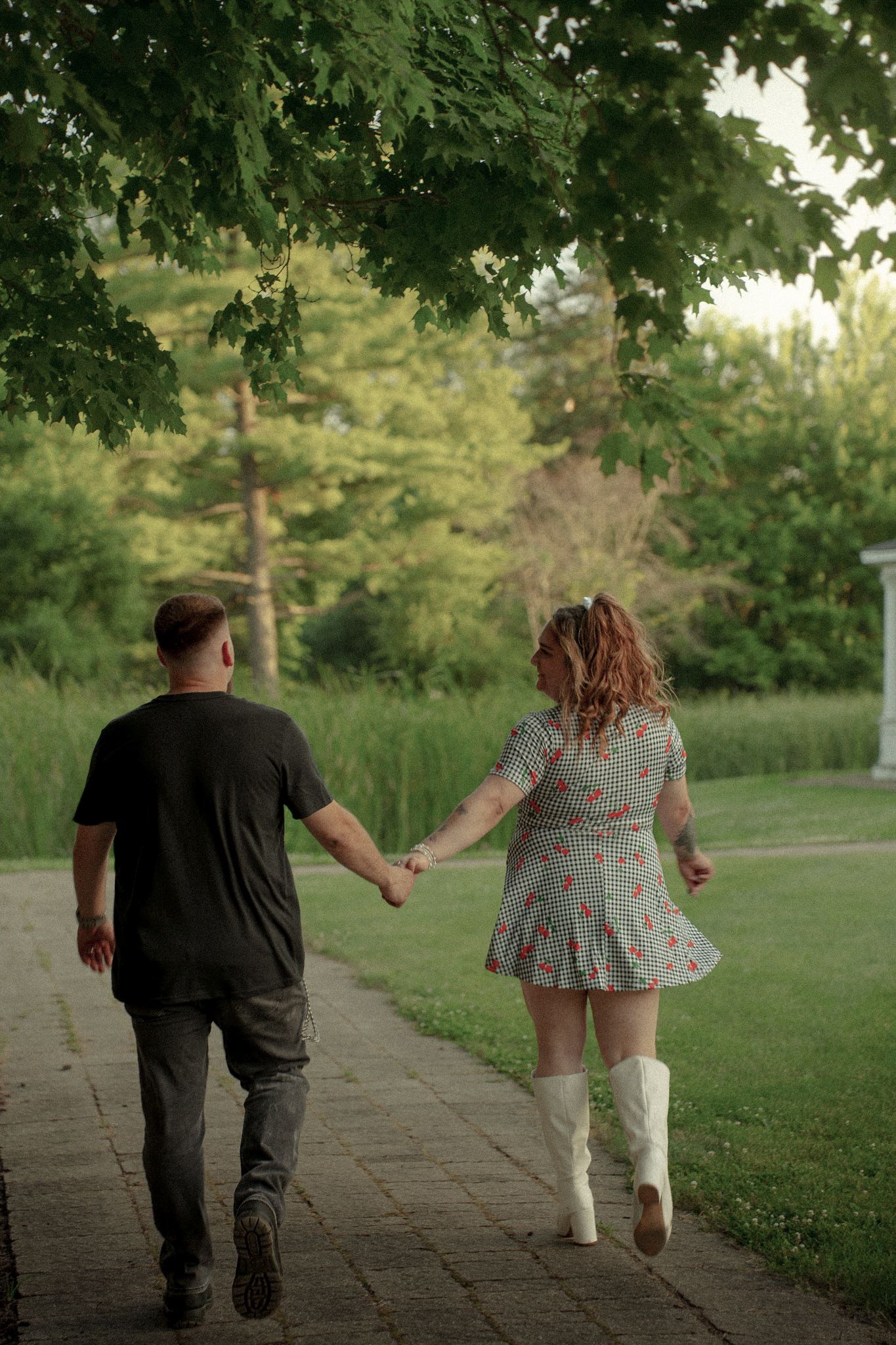 Couple walking hand in hand on a tree-lined path during golden hour.