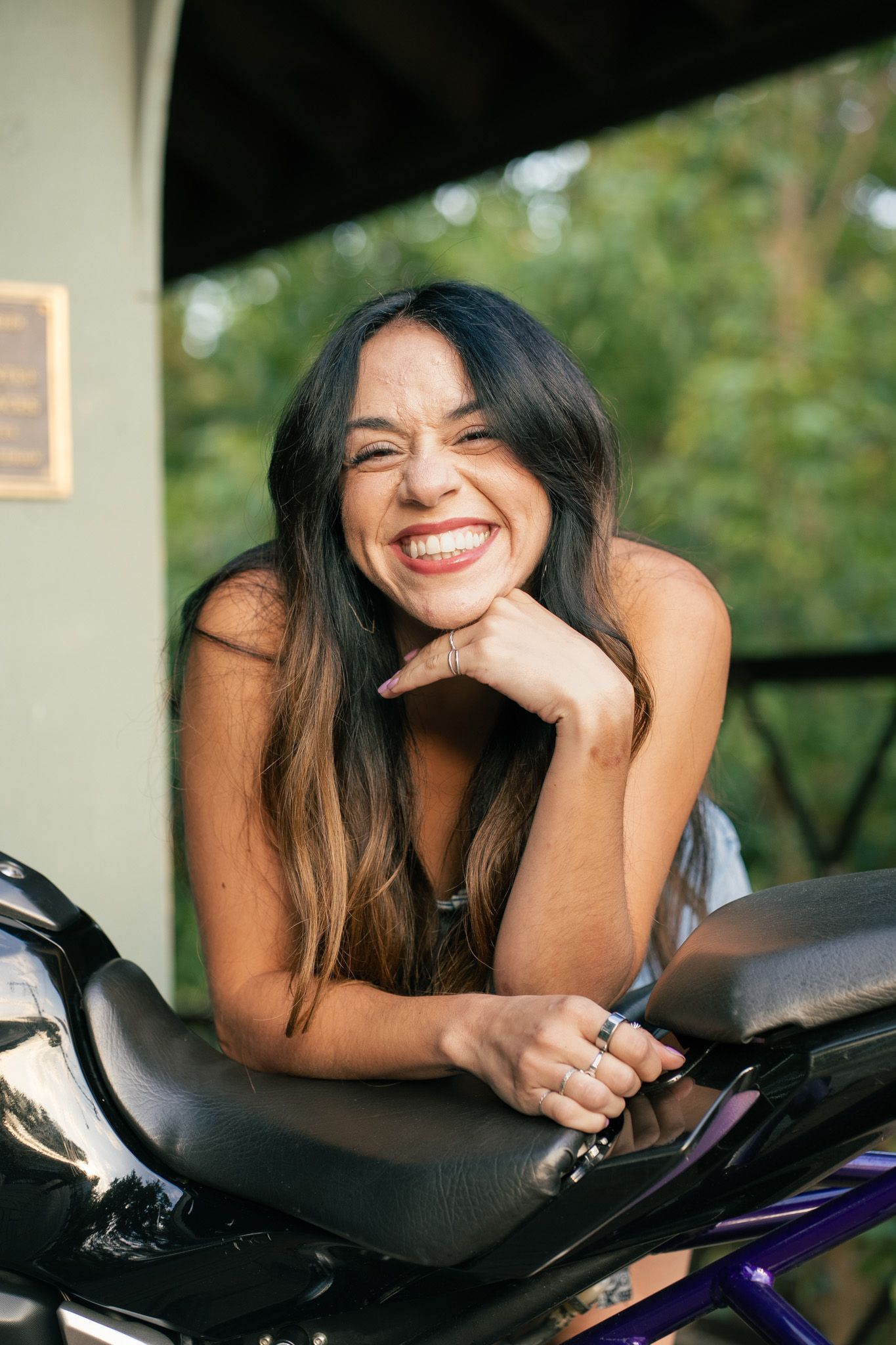 A person lounges on a black motorcycle while smiling outdoors.