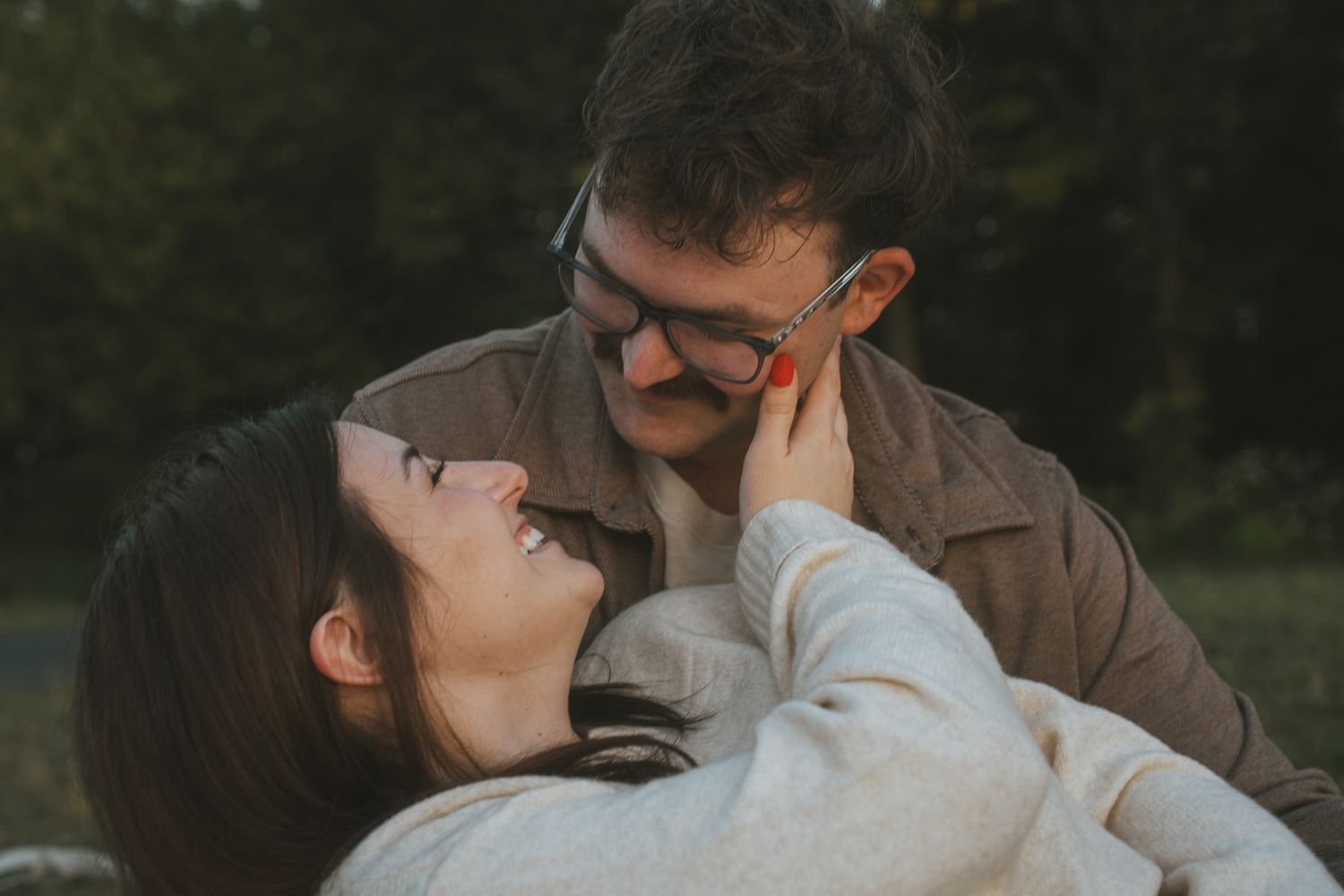A couple shares a romantic moment in a park setting with natural lighting and greenery in the background.