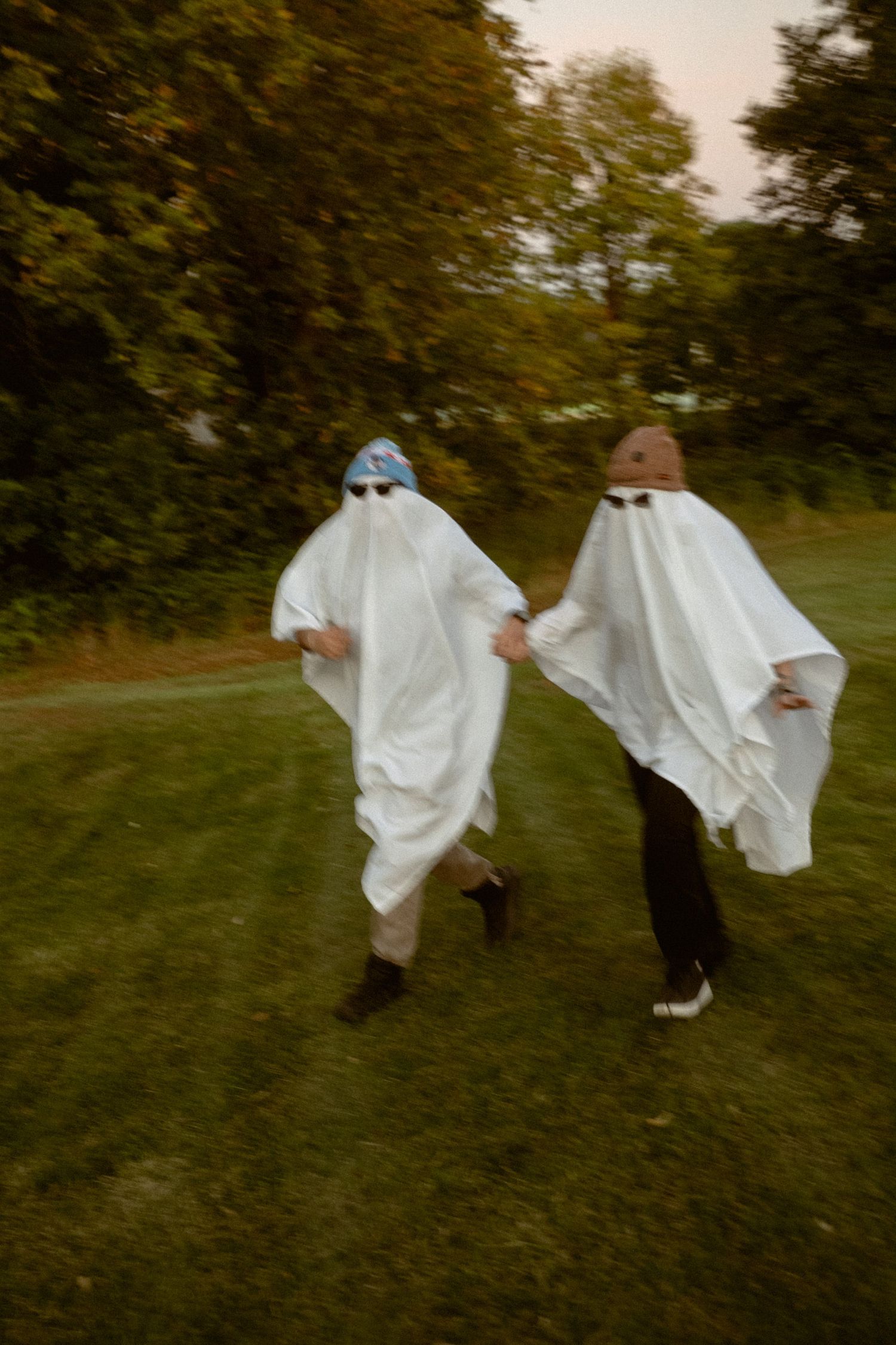 People dressed as ghosts in white sheets run and play in a grassy field at dusk.