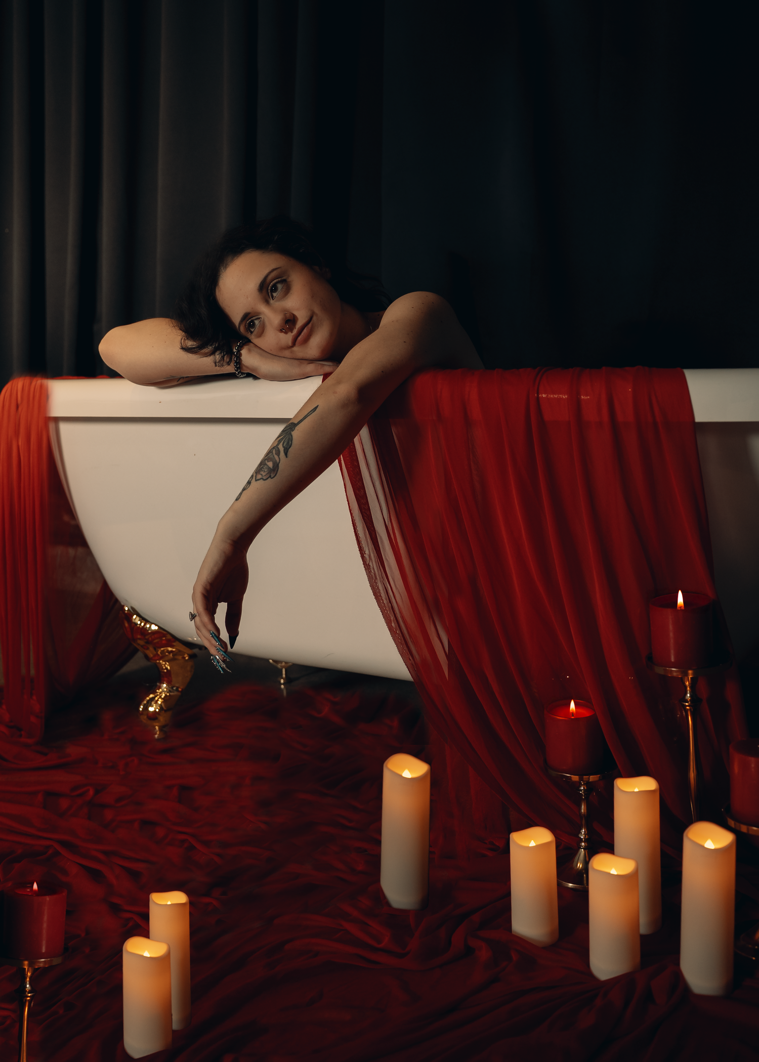 Bathtub scene with glowing candles and red curtains creating a moody, romantic atmosphere.