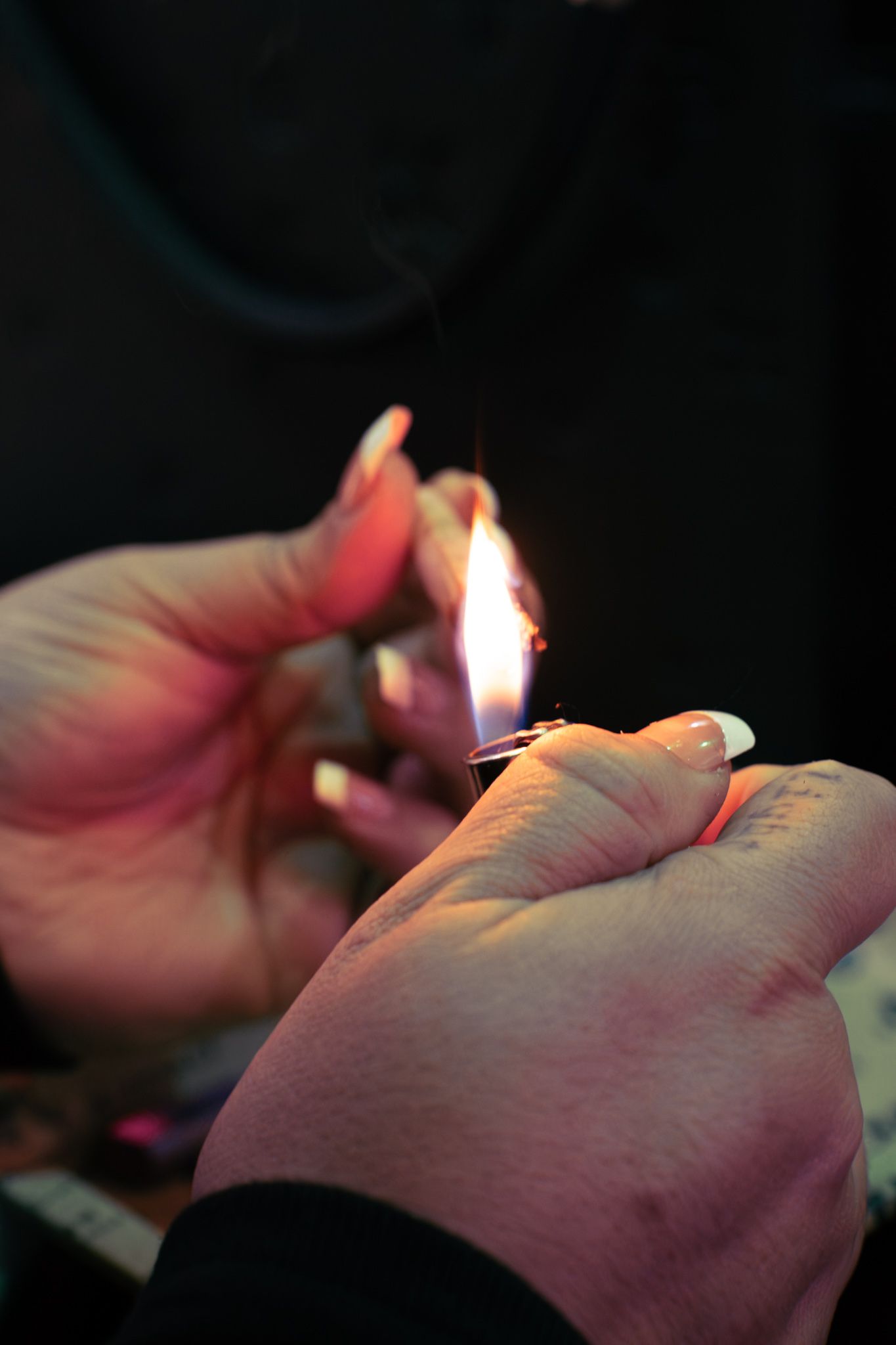 Hands lighting a cigarette lighter in the dark with warm glowing flame against black background.