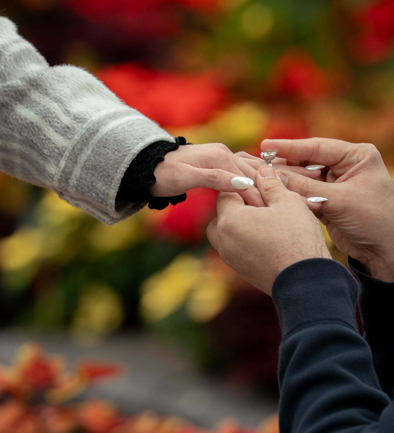 Close-up shot of hands exchanging a ring during an outdoor engagement or wedding ceremony.