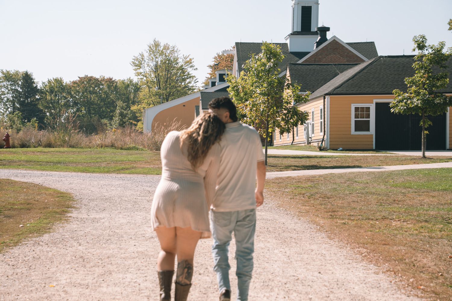 A couple walks together on a path with buildings visible in the background.