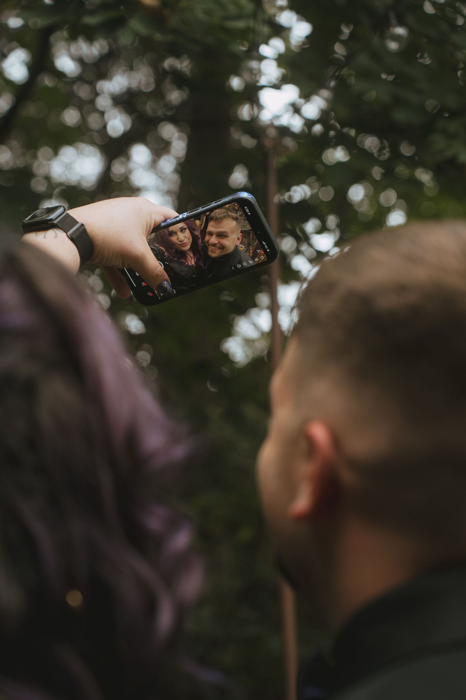 A phone screen captures a reflection of a couple taking a selfie together in nature.