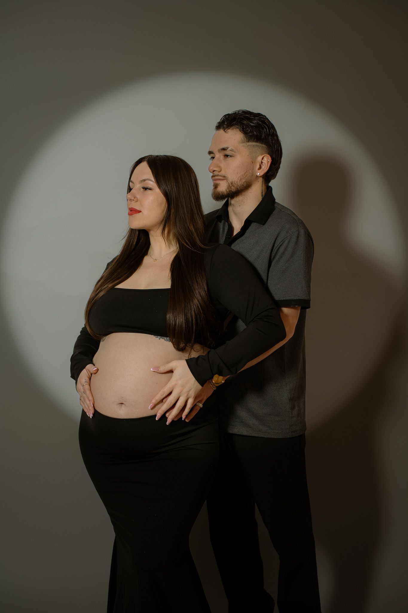 Intimate maternity photoshoot featuring silhouetted couple in black and grey against neutral backdrop.
