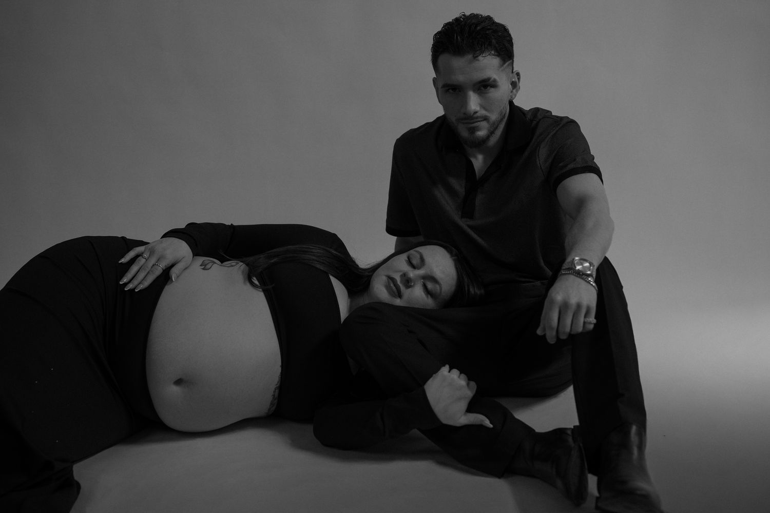 A dramatic black and white maternity portrait with a couple in dark attire.