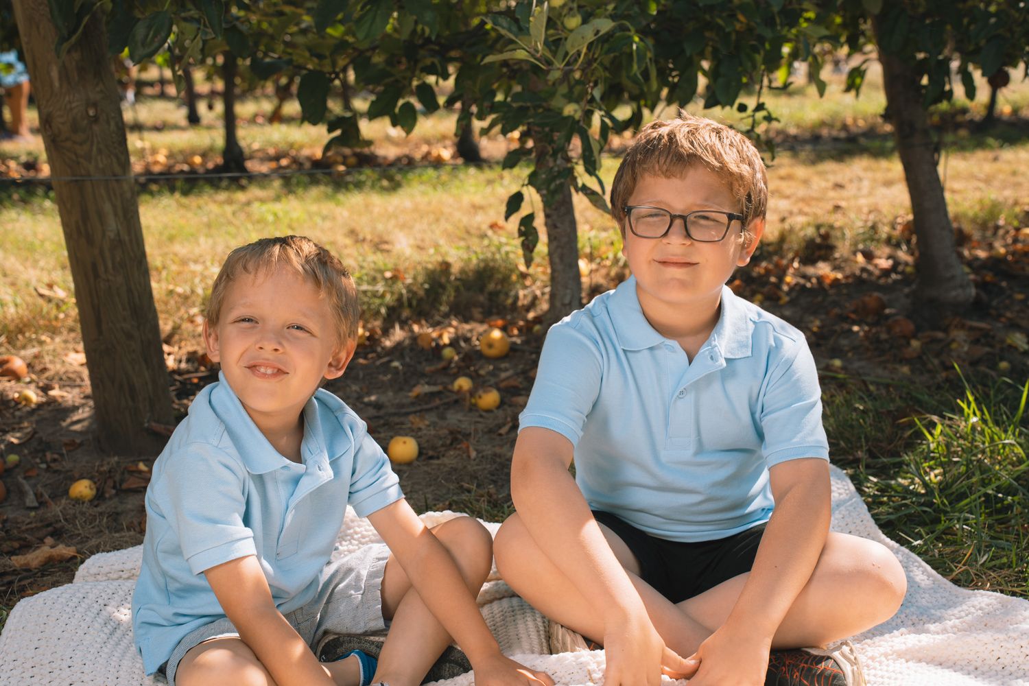 Boys in light blue shirts sitting together outdoors in autumn setting.