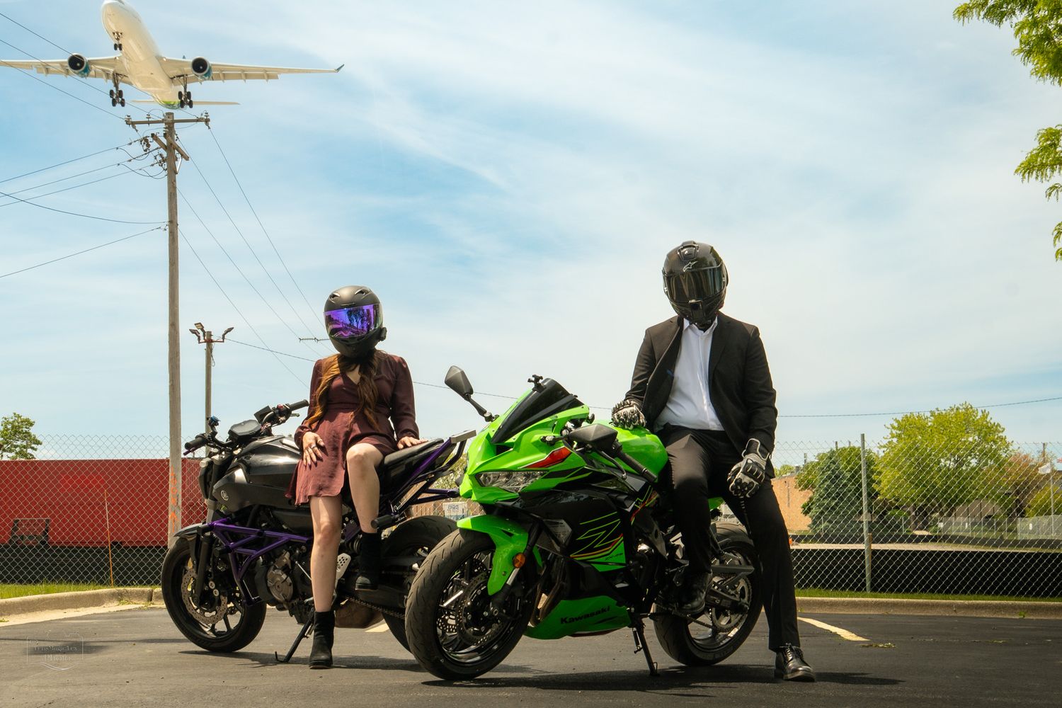 Motorcycles parked in parking lot with riders in protective gear under blue sky.