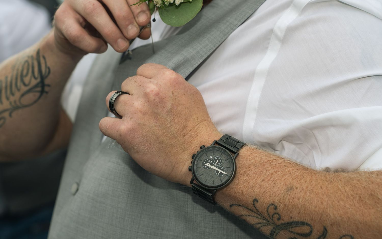 Close-up of tattooed hands adjusting clothing while wearing a modern watch.