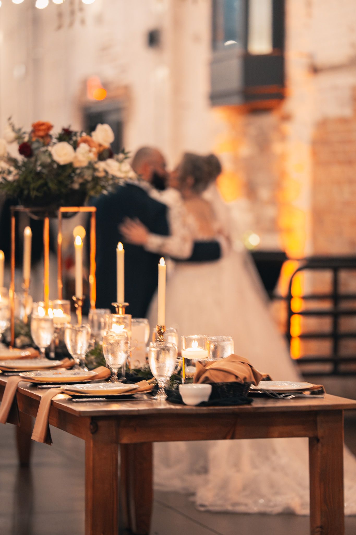 Elegant wedding reception table with glowing candles and place settings in warm lighting.