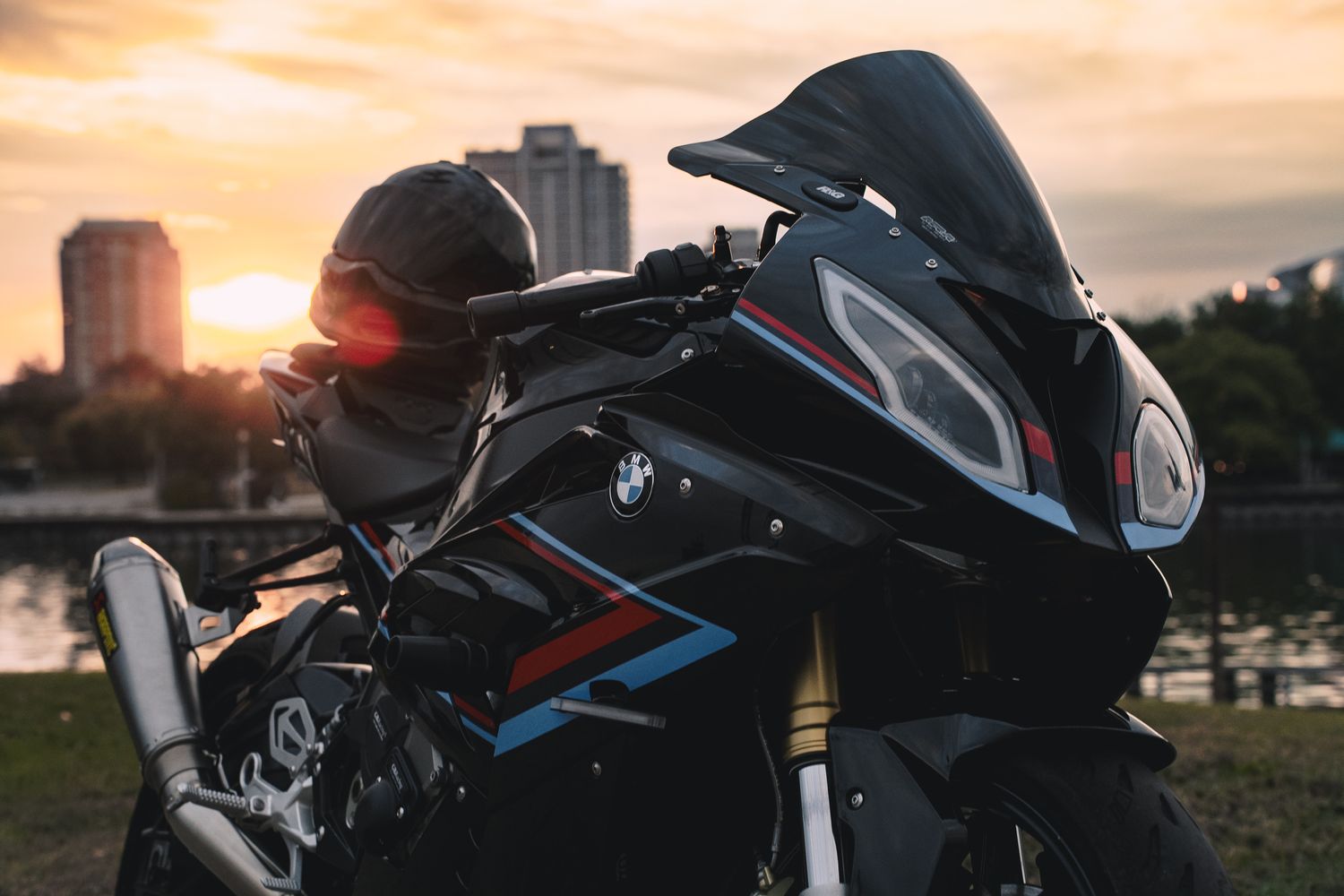Motorcycle silhouetted against a vibrant orange sunset with palm trees in the background.