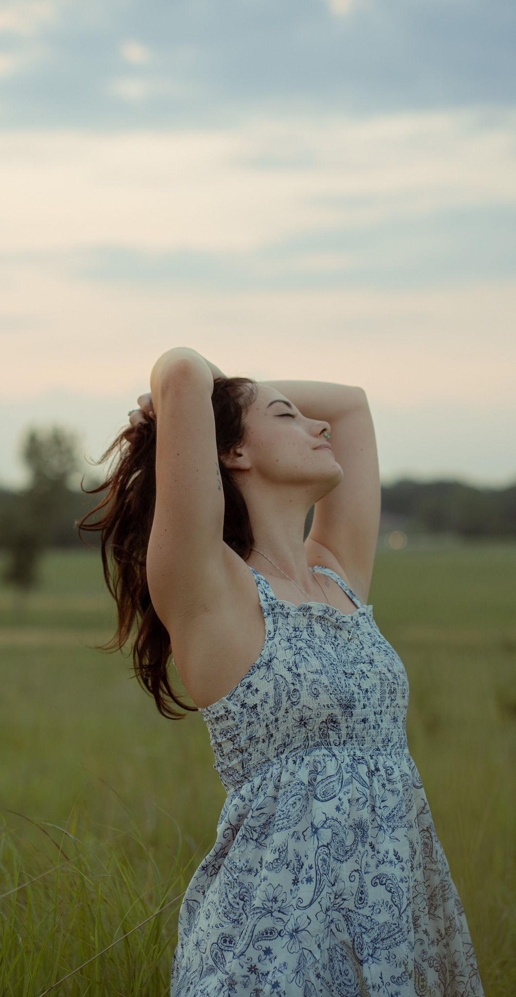 Figure in patterned dress poses expressively in a summer field at golden hour.