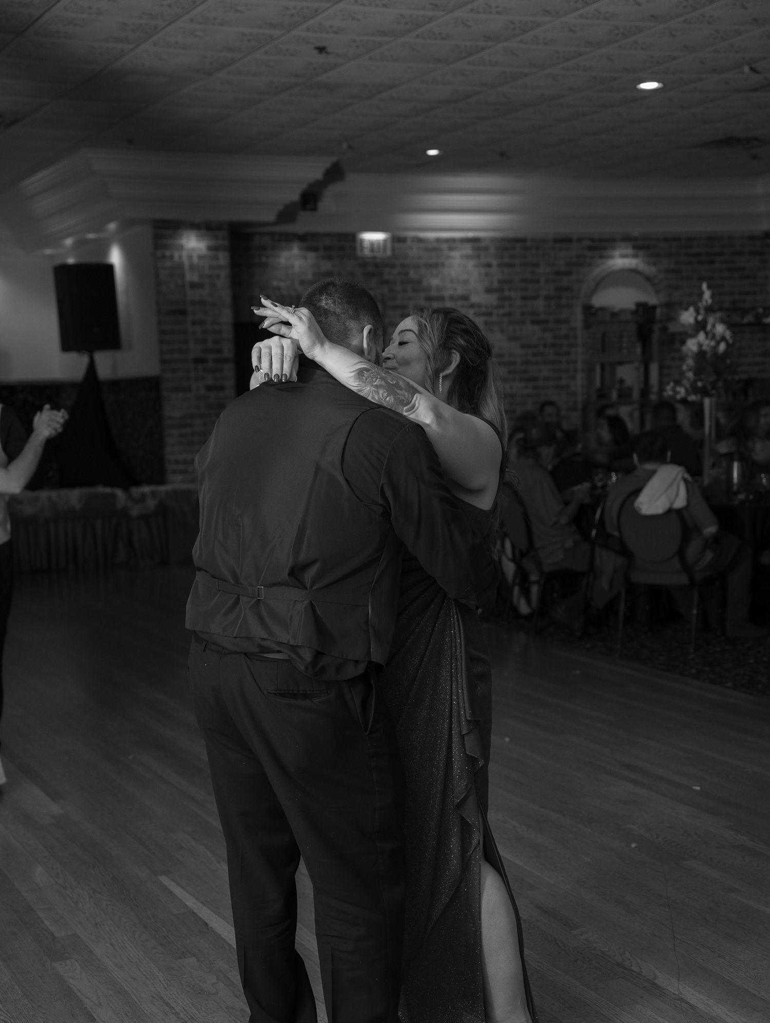 A couple shares an intimate slow dance together on a wooden floor in a dimly lit room.