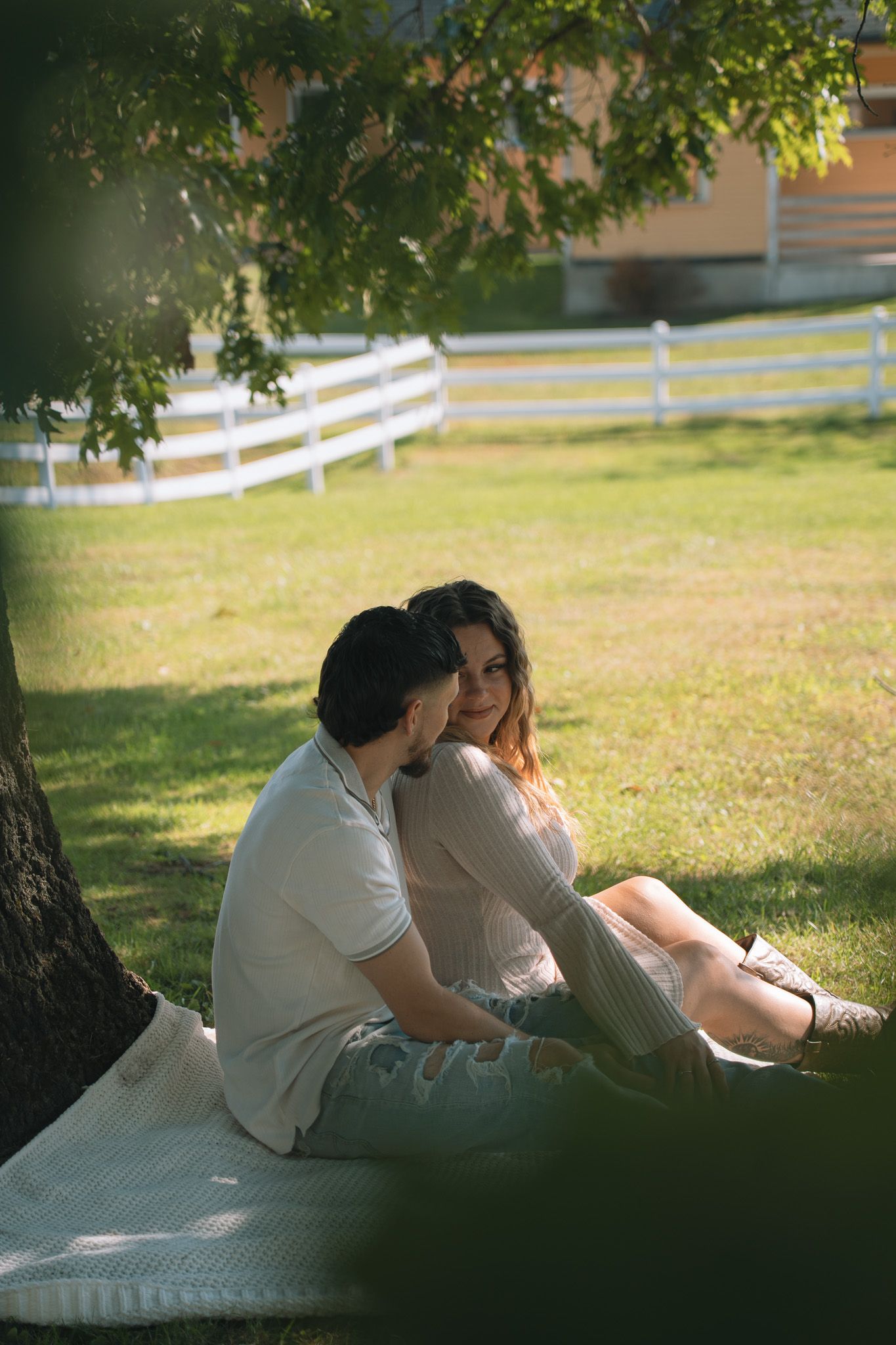 A couple shares intimate moments under tree shade during their photoshoot.