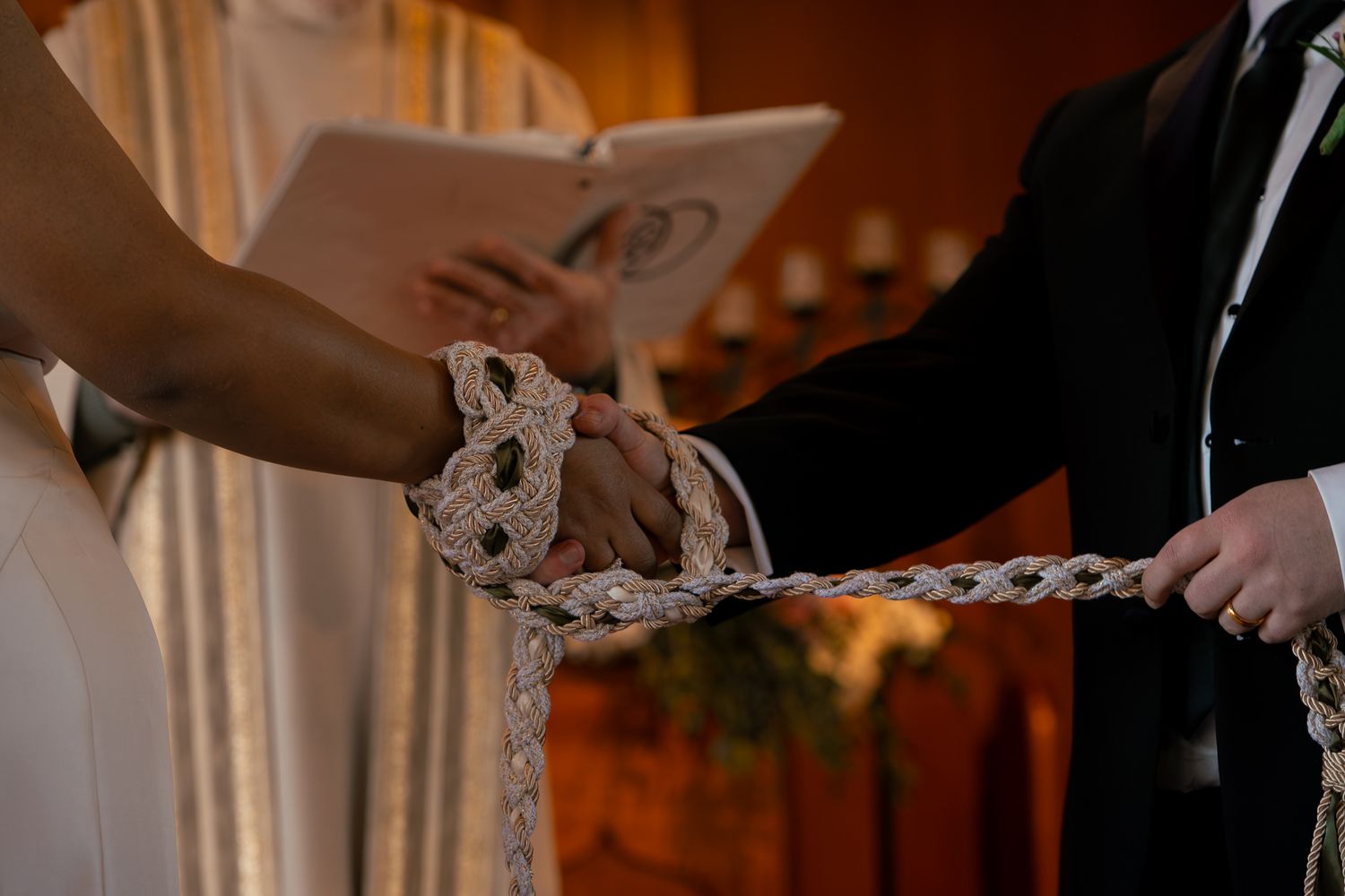 Couple's hands bound together with decorative rope during a handfasting wedding ceremony ritual.
