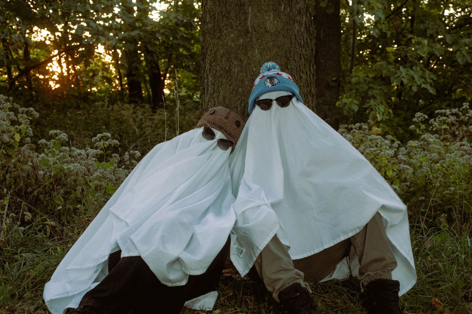 Ghostly figures in white sheets pose dramatically against trees in fading daylight.