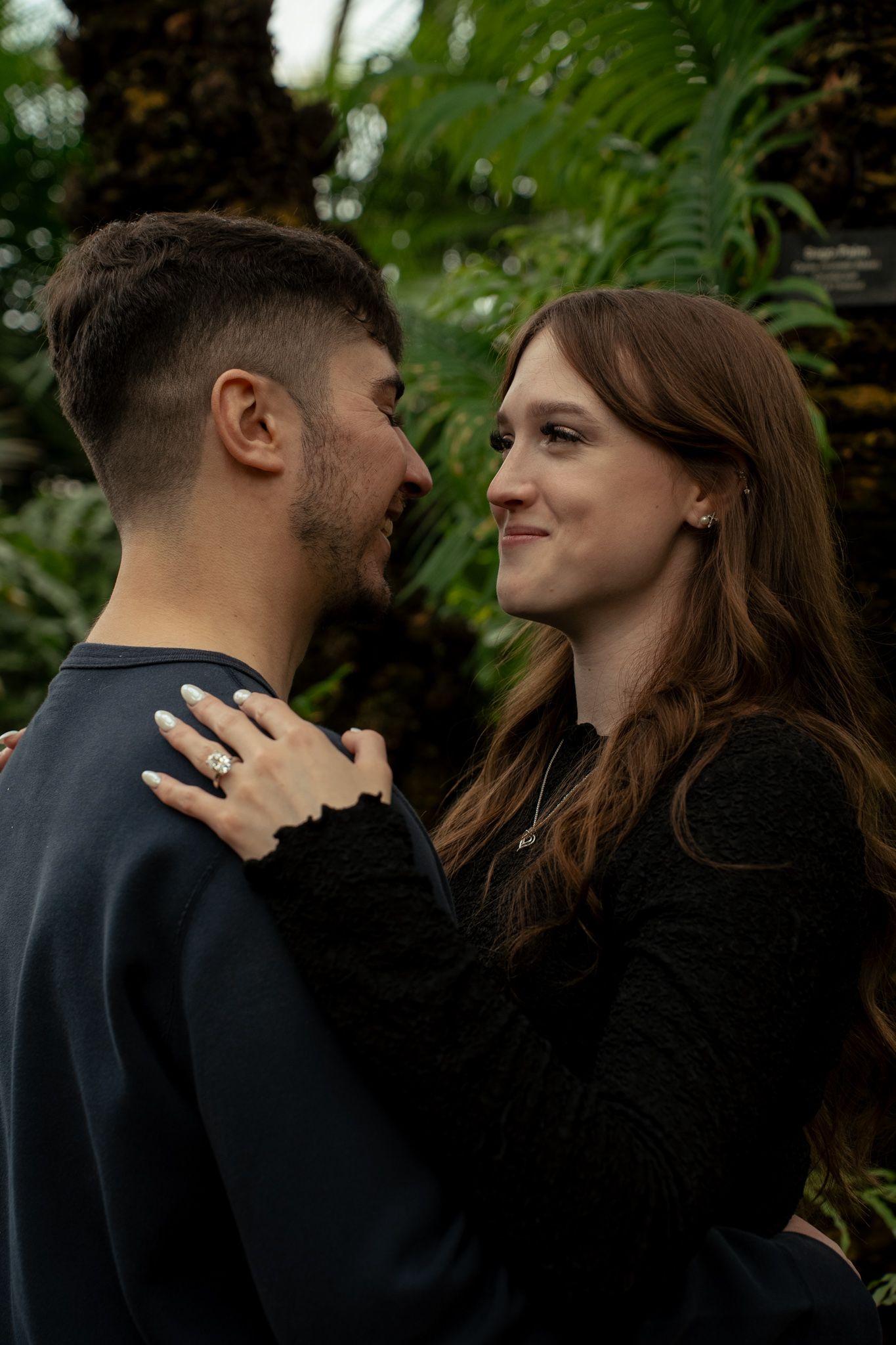 A romantic couple in dark clothing share tender moments together in a garden setting.