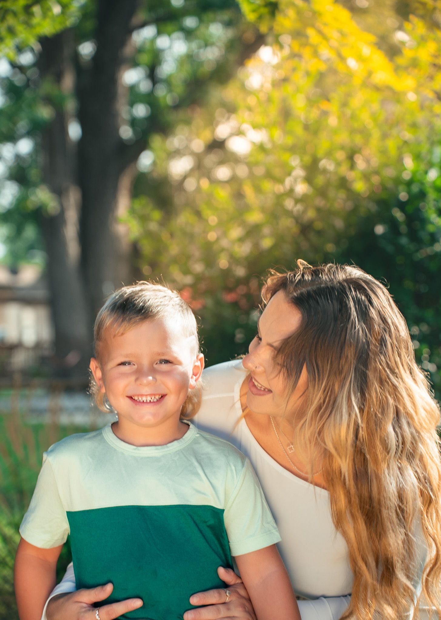 A heartwarming outdoor family moment captured in natural sunlight with green and yellow foliage.