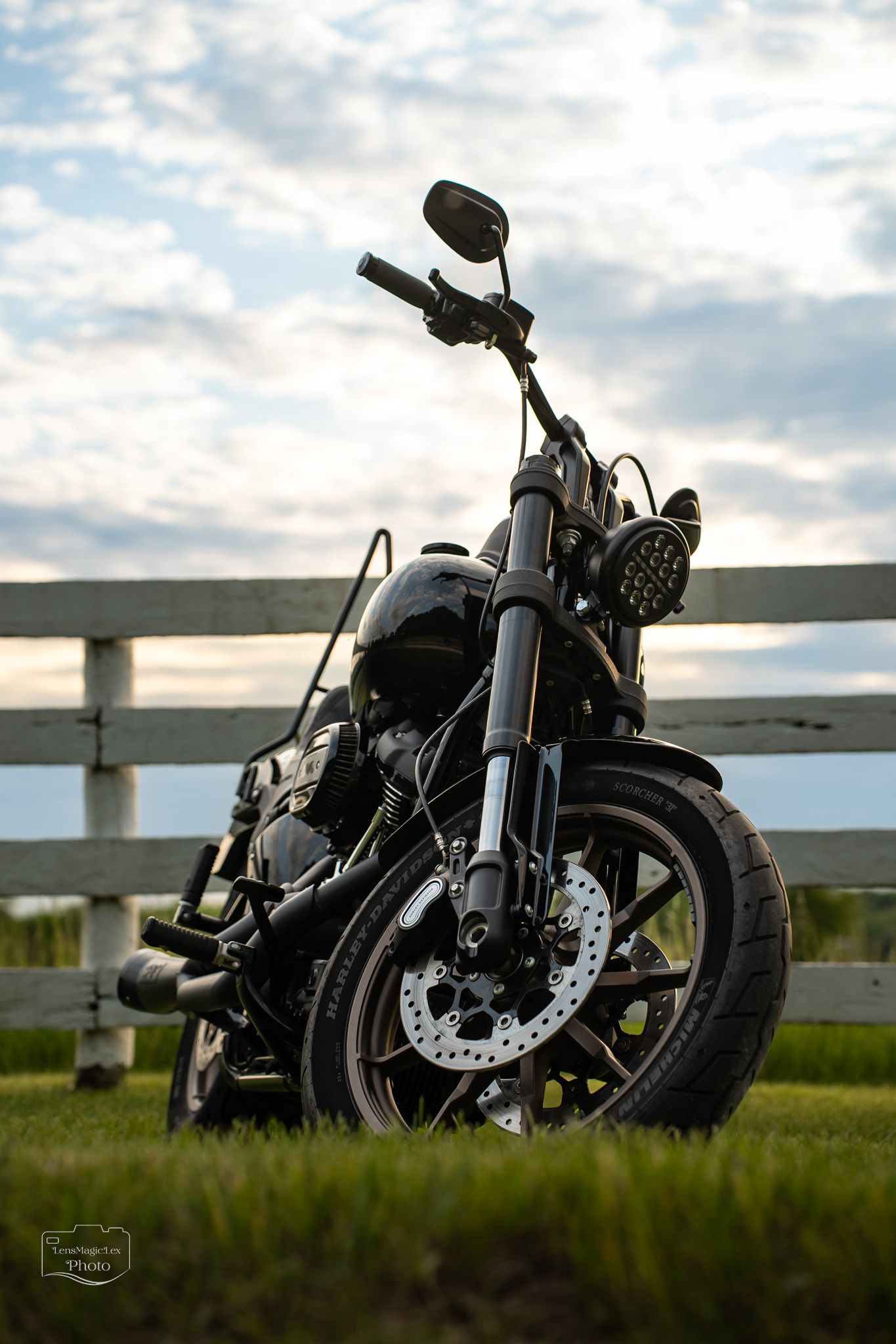 Black motorcycle parked on grass against white fence during sunset.