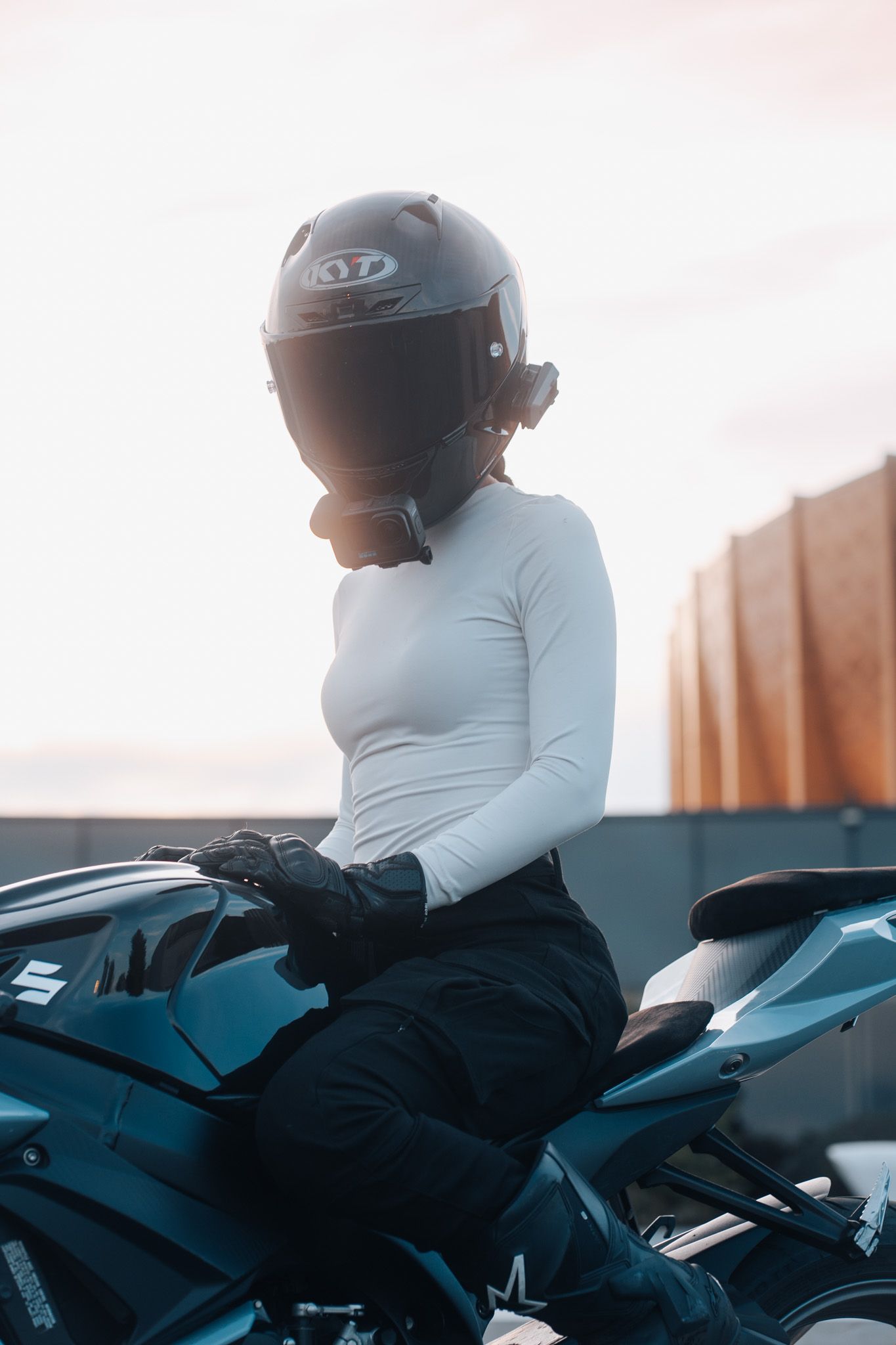 Motorcycle rider in white shirt and black helmet leans forward on a sleek sport bike.