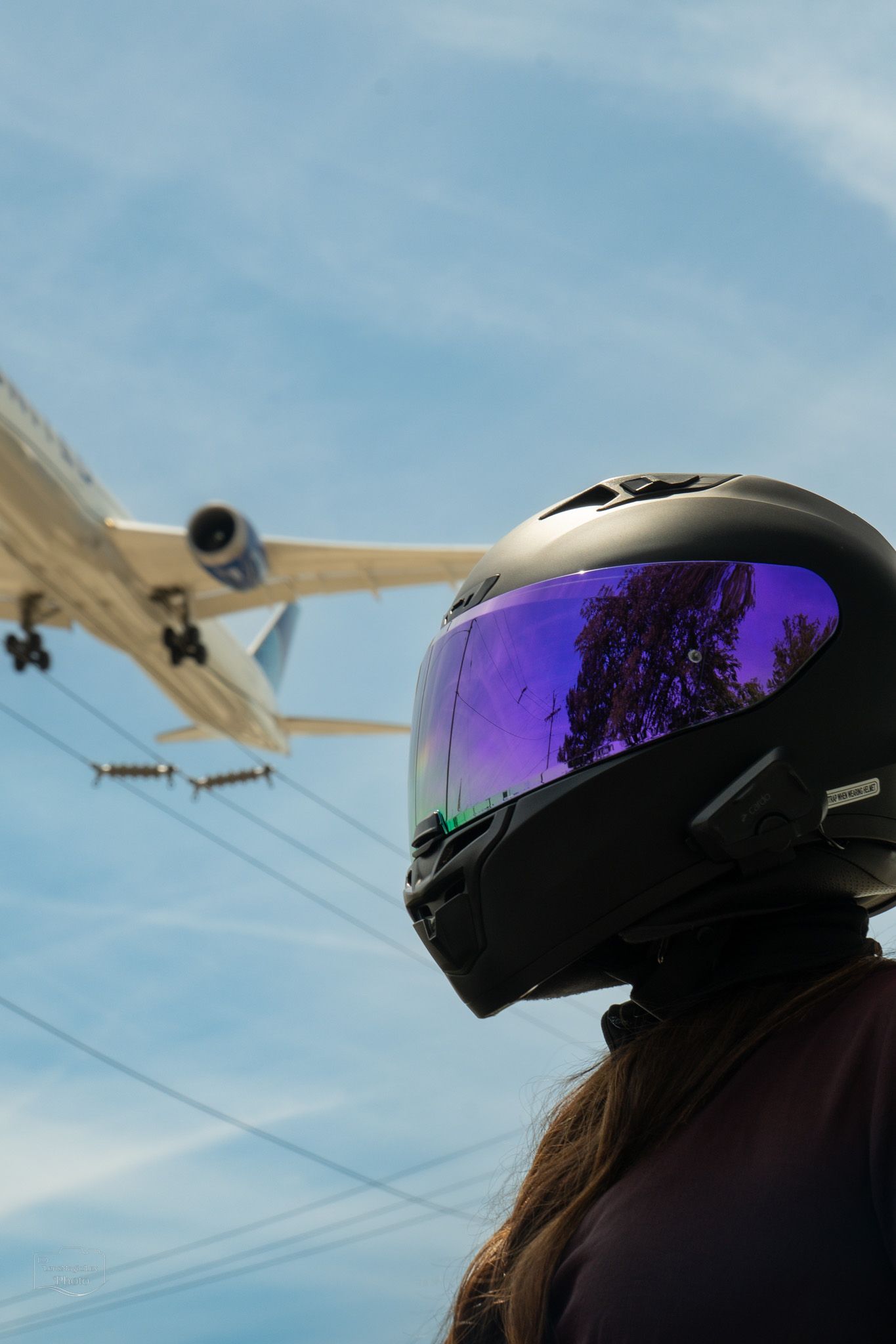 Helmet with purple reflective visor against blue sky with power lines.