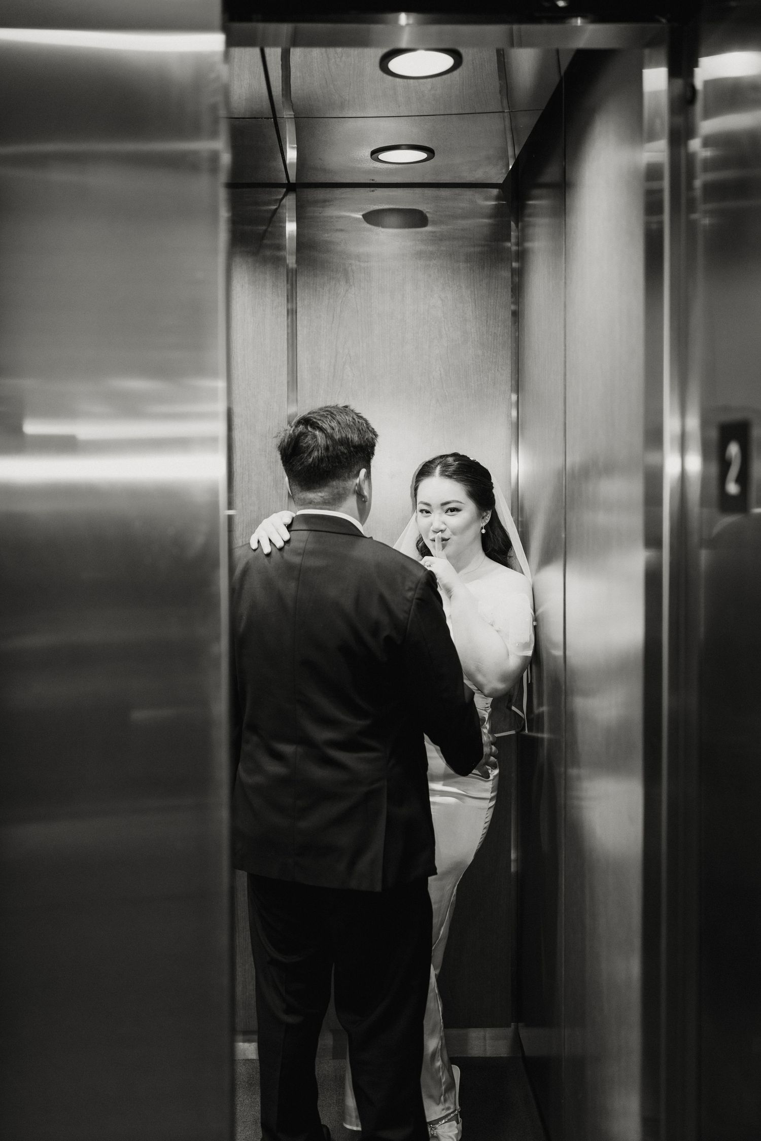 Bride holding up index finger to lips as elevator closes
