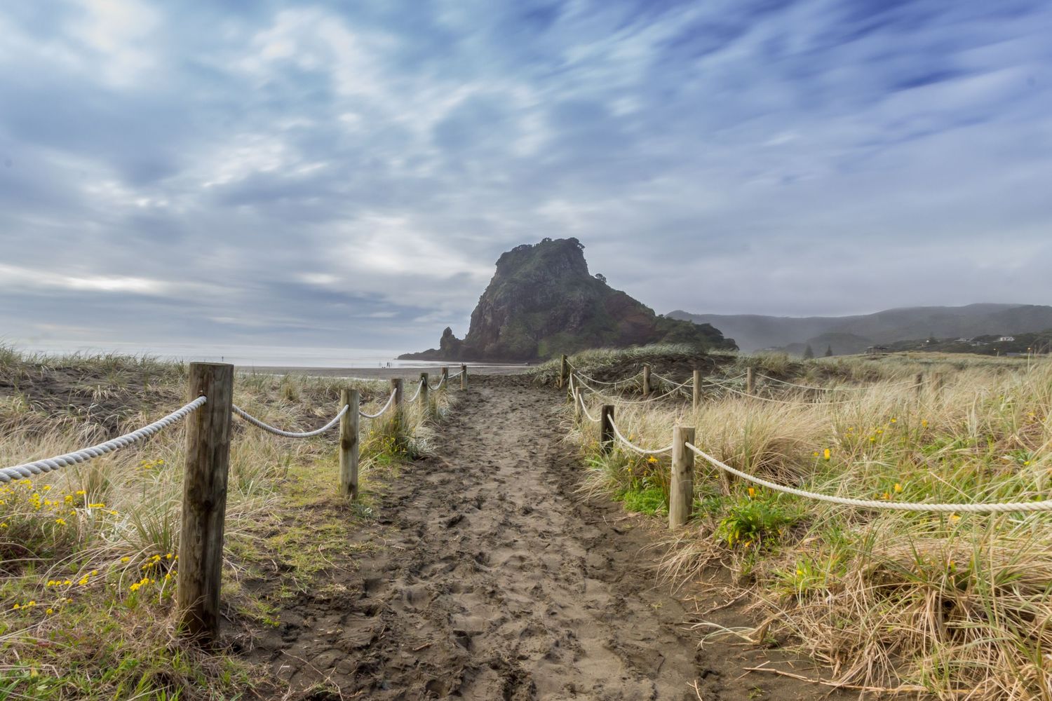Scenic coastal path with rope fence leading to mountain views in the distance.