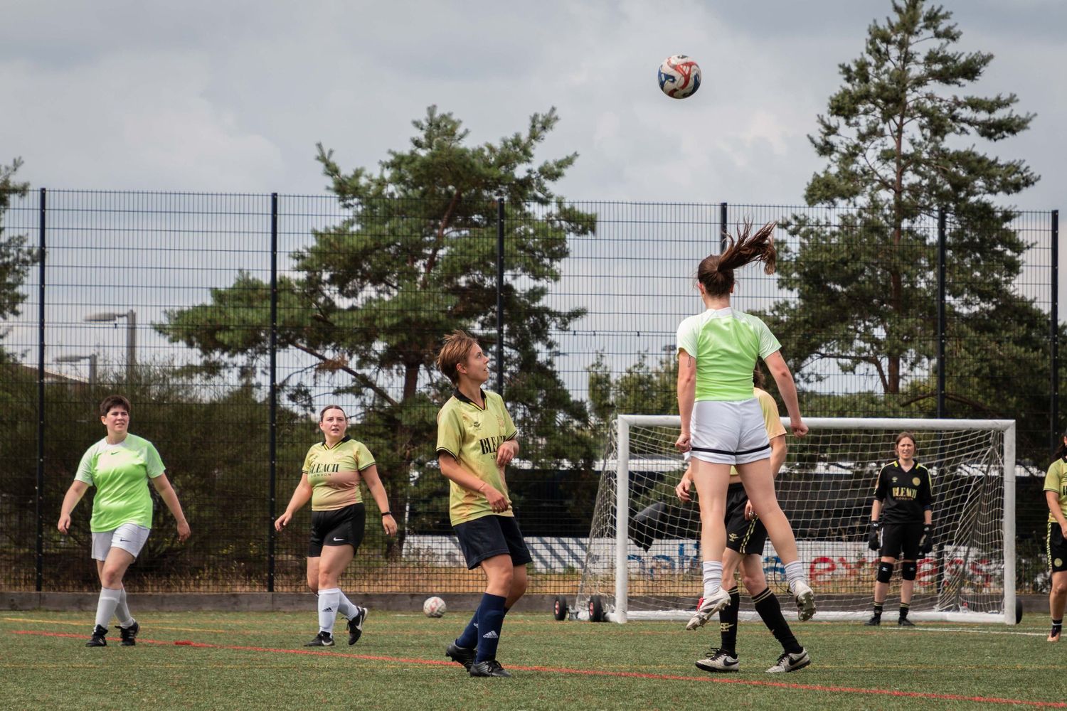 Soccer players engaged in a scrimmage match on a sunny day with goal posts visible.