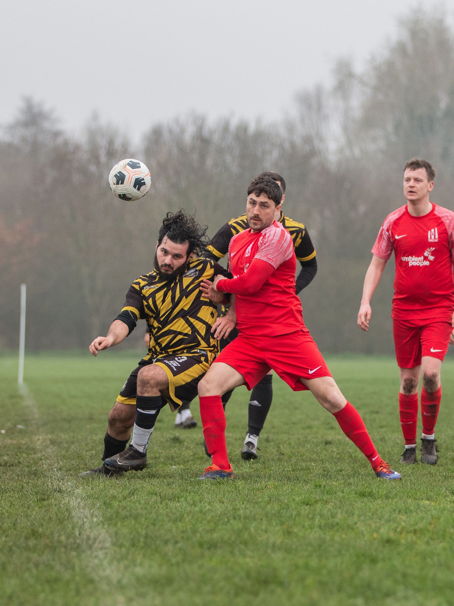Soccer players in red and black-yellow uniforms compete for possession of the ball on a grassy field during a match.