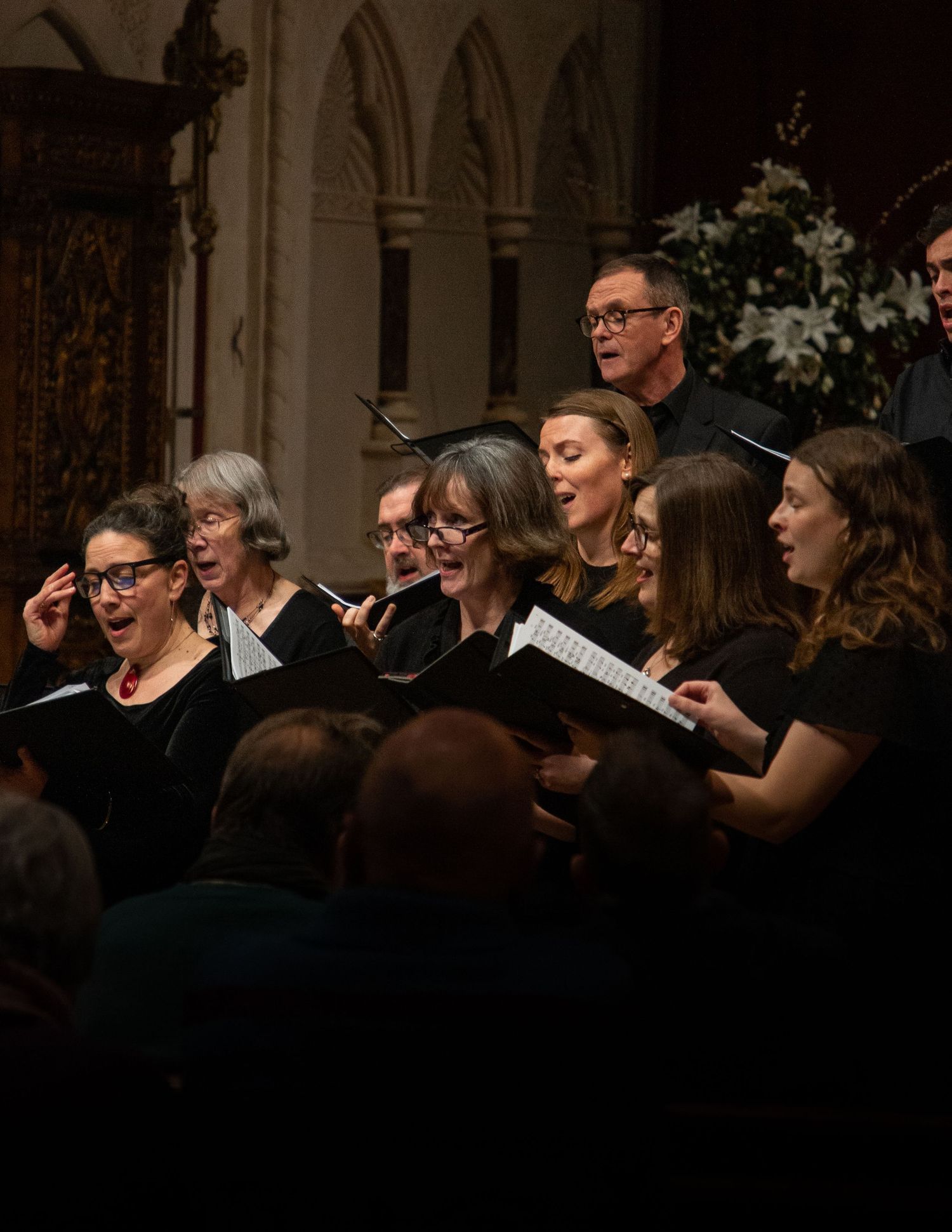A choir performs in formal black attire inside a church with gothic arches and dramatic lighting.